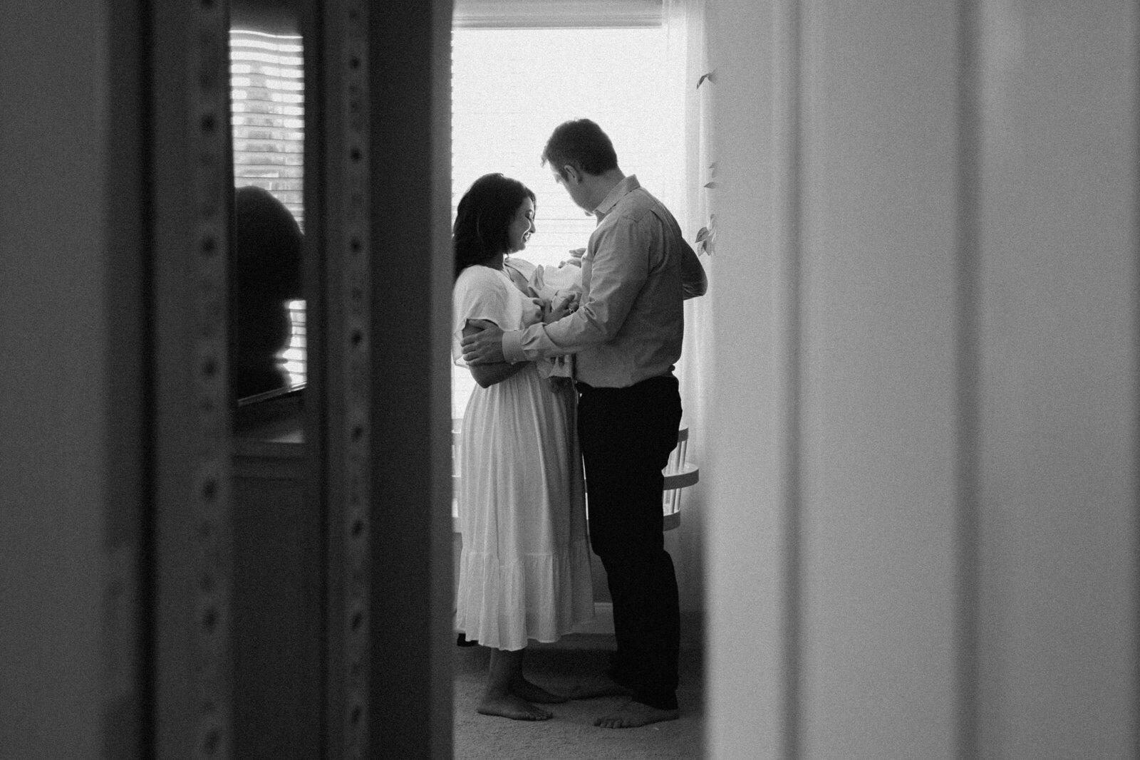 A mom and dad stand close while looking down at their newborn son