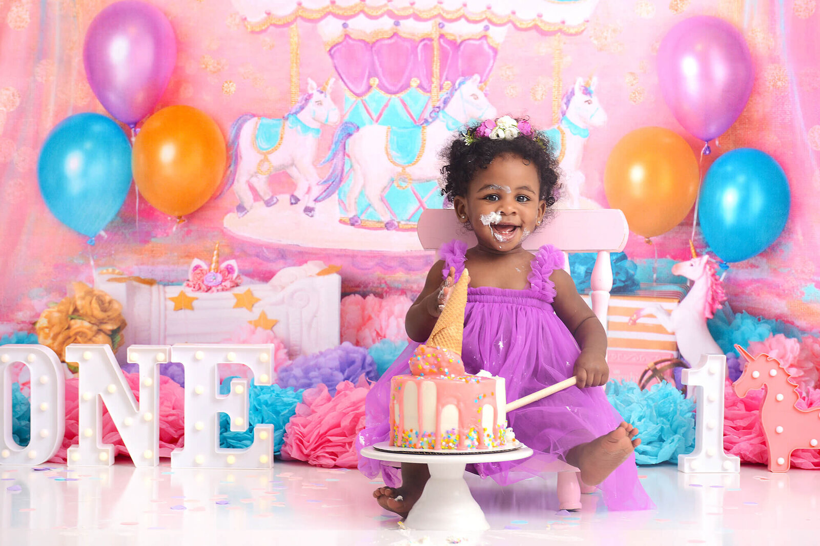 baby girl smiles while destroying her birthday cake  at her first birthday photoshoot