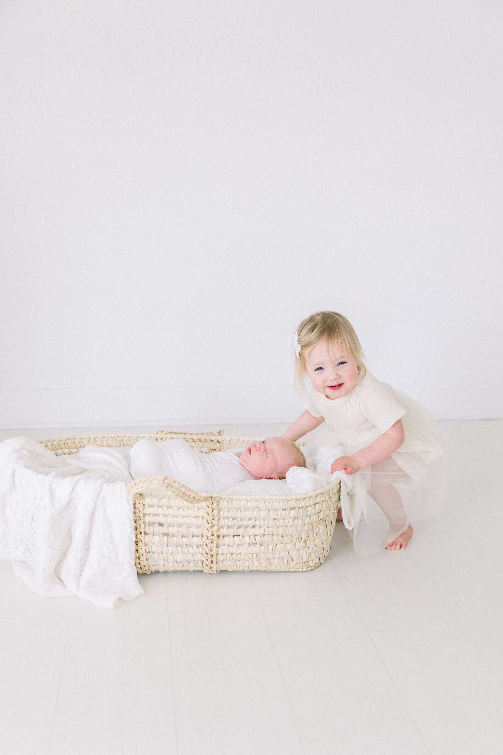 Older sister looking of baby brother in basket in studio taken by Family Photographer Sacramento Kelsey Krall