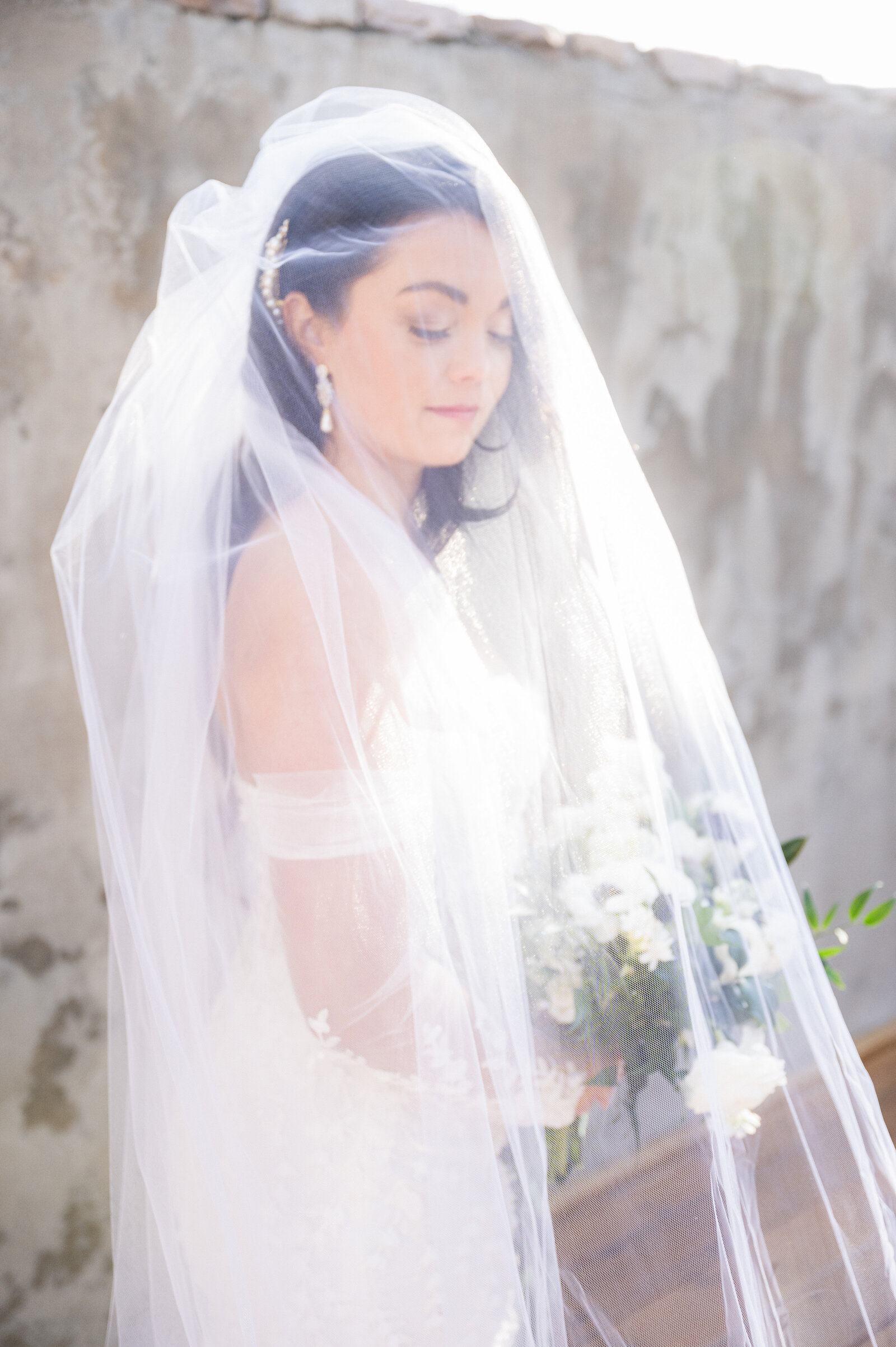 Bride poses for photo with her veil draped over her head at The Oaks at Plum Creek in Castle Rock, Colorado.