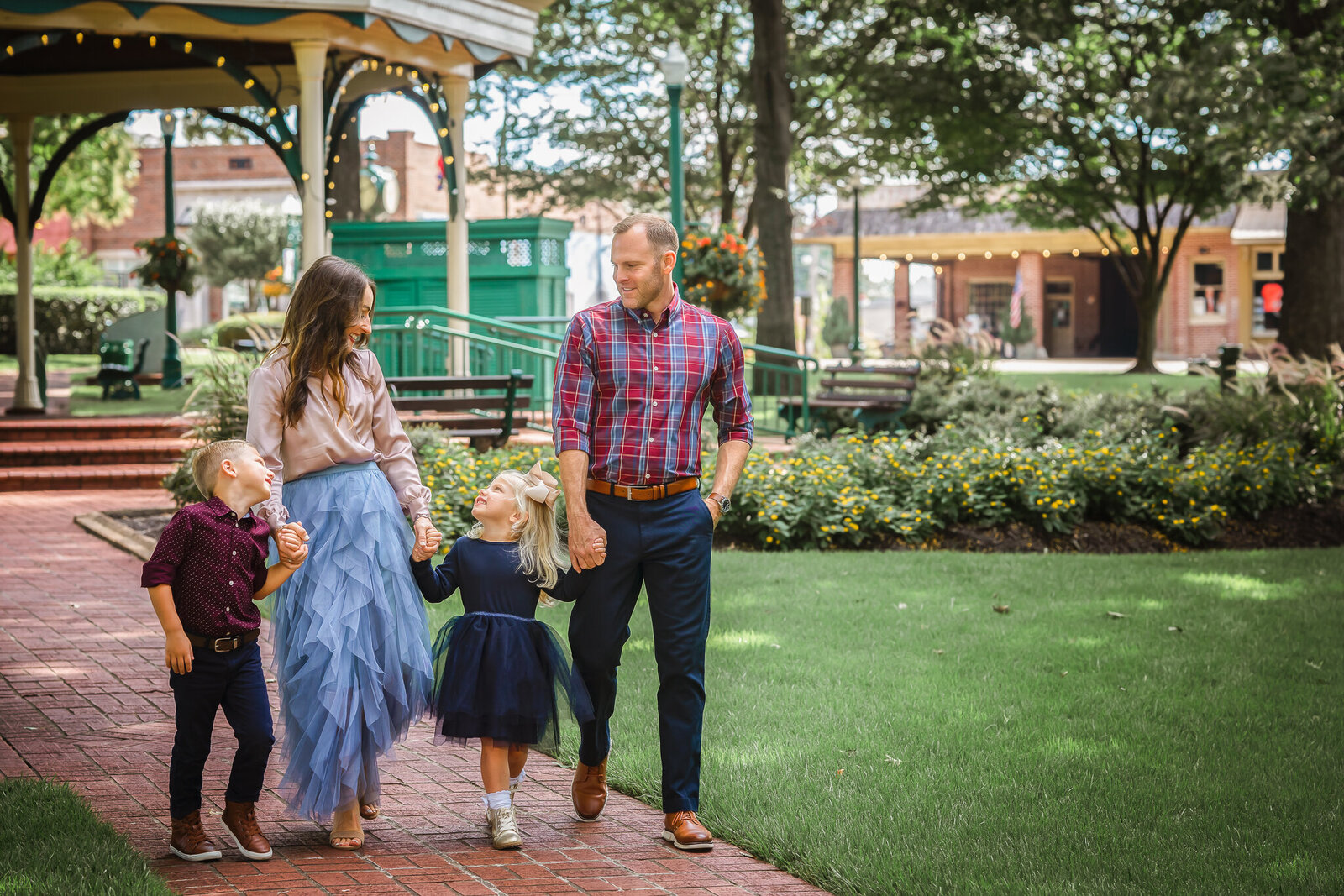 A family of four holds hands while they walk through the park at their family photo session,