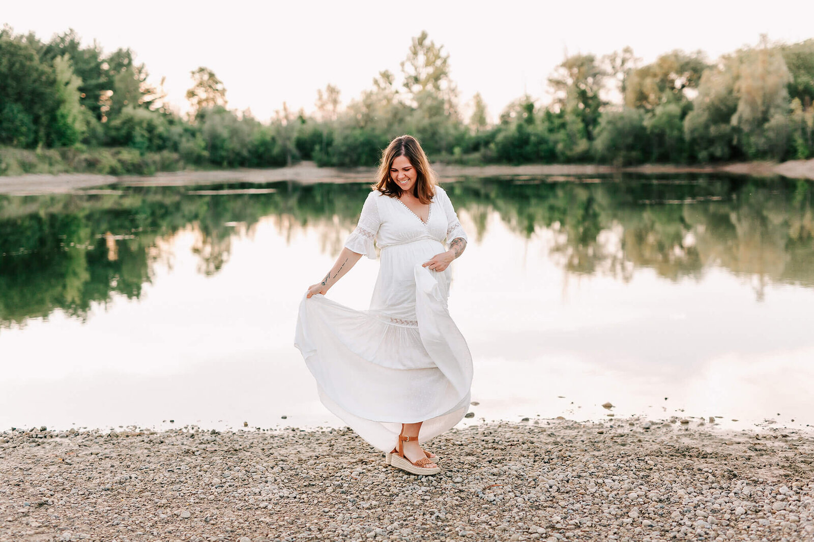 Pregnant woman  in a white Baltic Born dress, dances in front of the water during her photoshoot