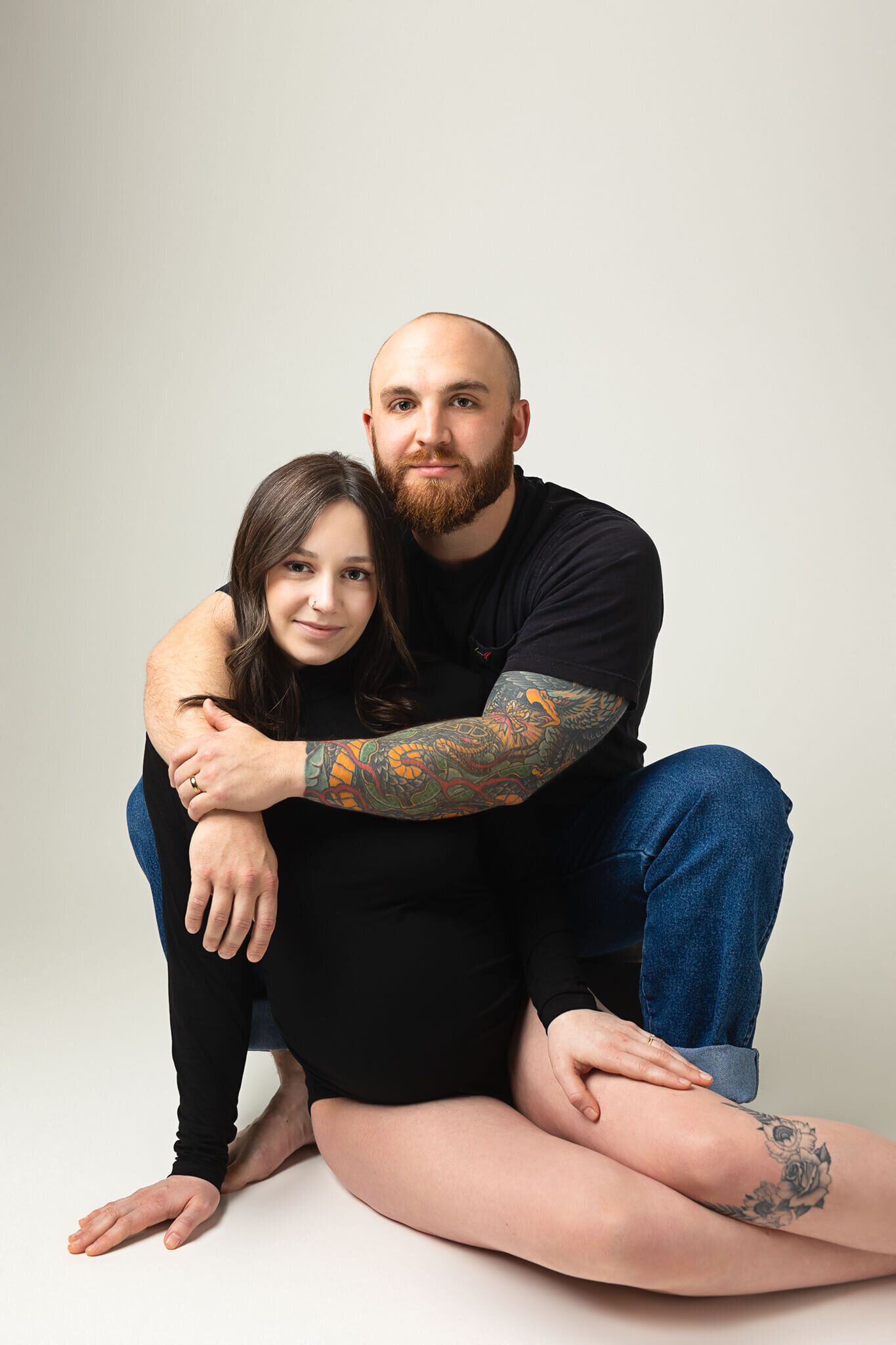 Portrait of pregnant woman posing with her husband on a white backdrop wearing a black bodysuit in austin photography studios