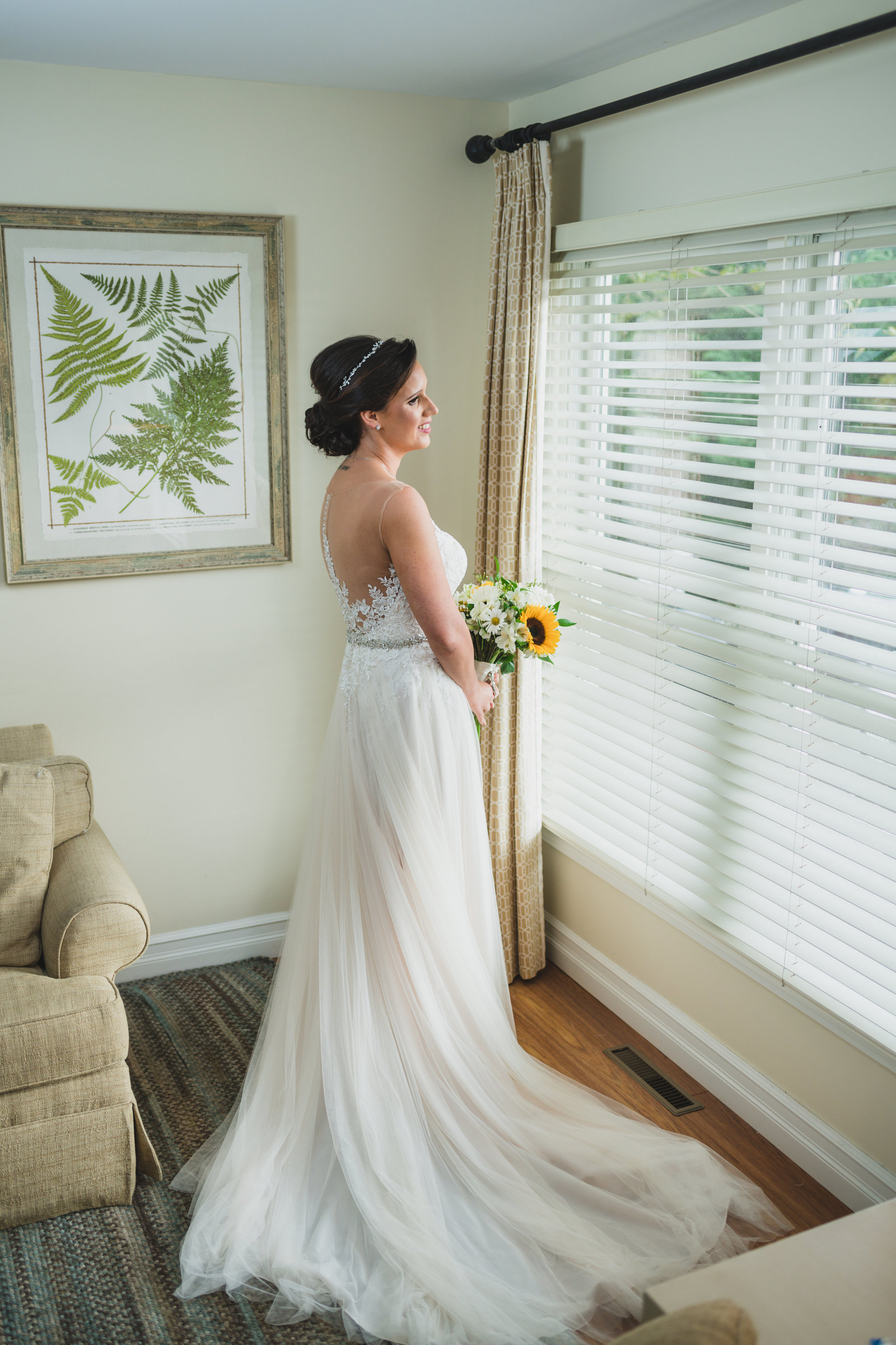 photo of bride in gown holding bouquet and looking out the window from wedding at Three Village Inn