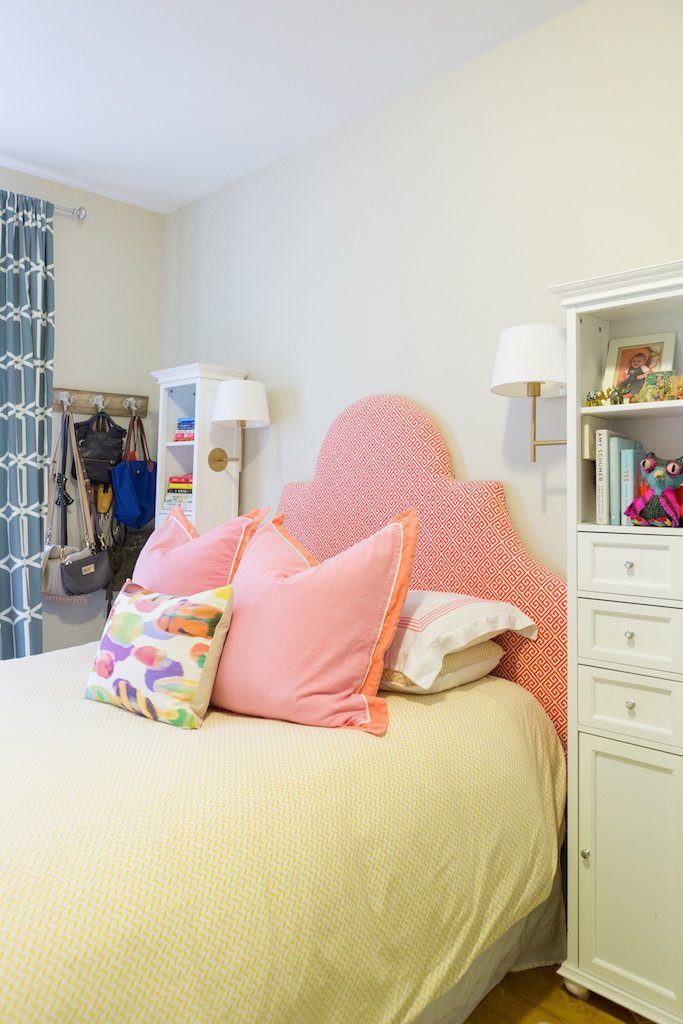 A bed with a pink and orange patterned headboard and pillows.