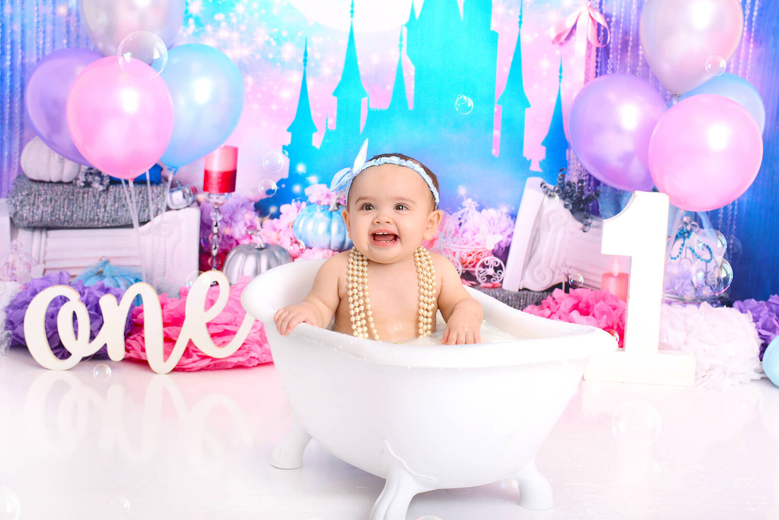 baby girl smiles in a milk bath at her 1st birthday photography shoot