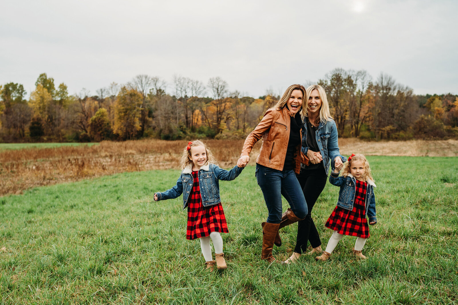 two moms laugh in a field with their daughter in Autumn