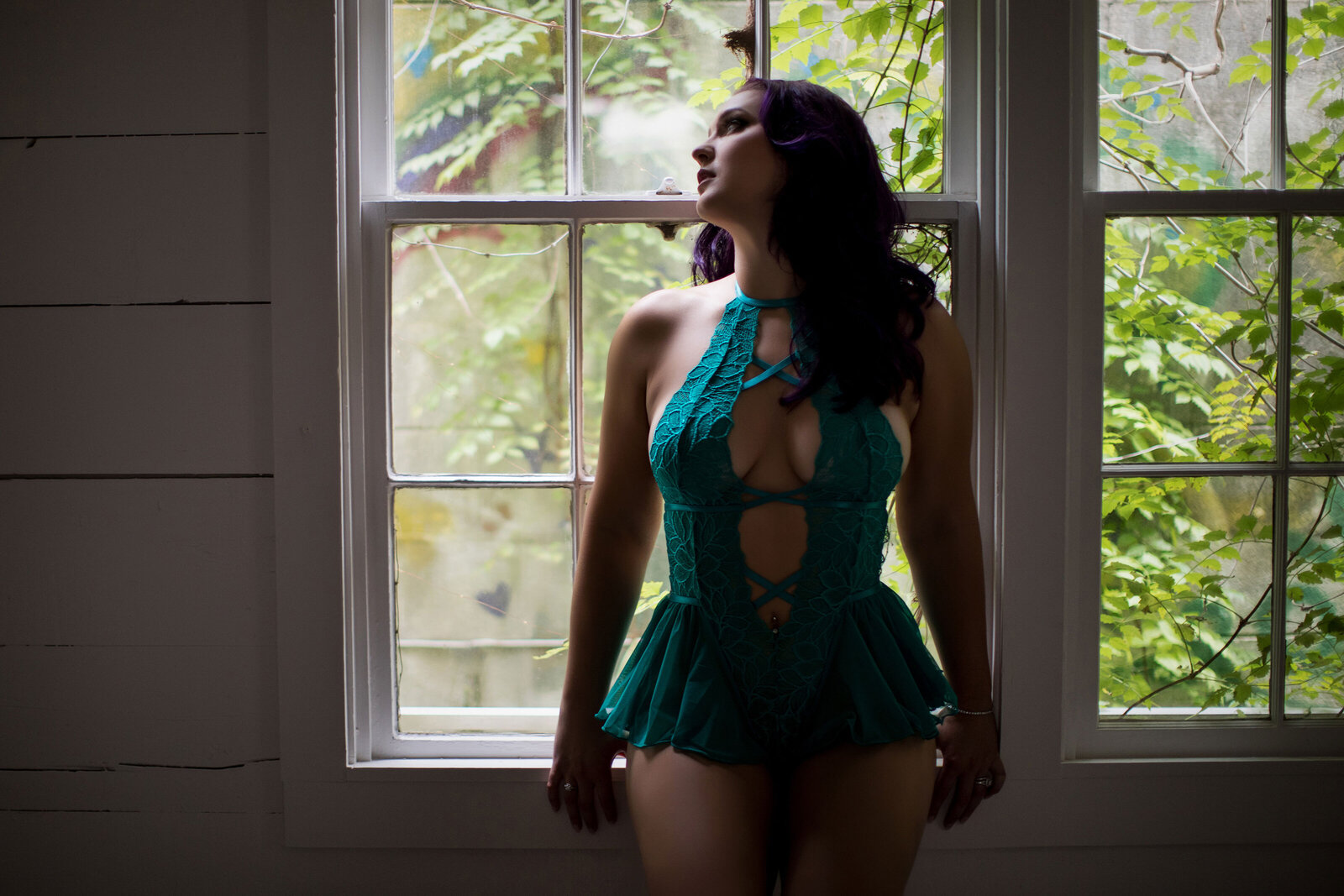 Woman wearing green lingerie standing in front of window with greenery in Baton Rouge boudoir studio.
