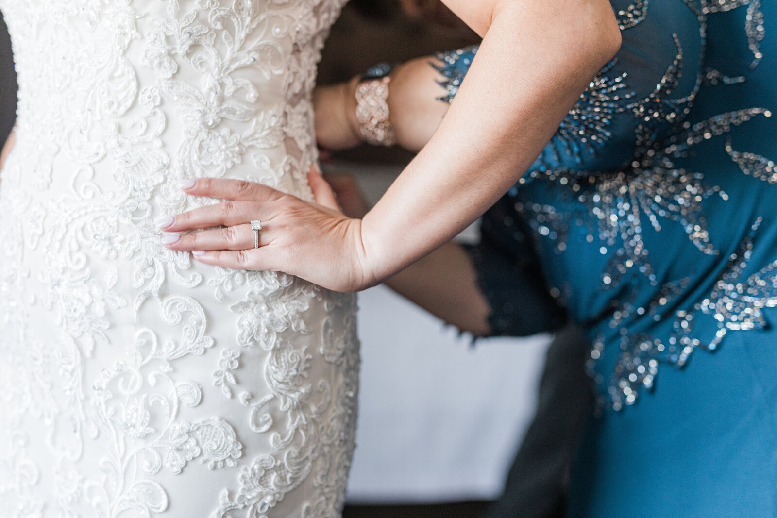 close up photograph of a bride with her hand on her hip and her mother buttoning her gown
