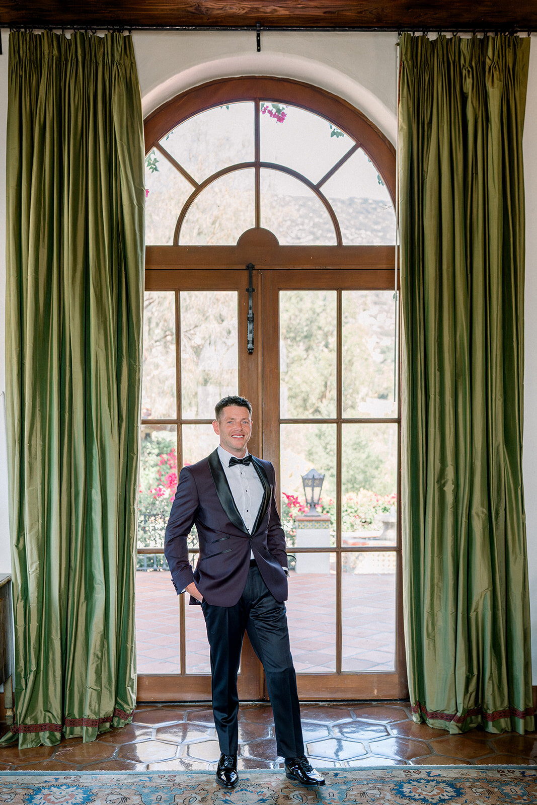 Groom framed by dramatic green velvet curtains in a refined portrait at Hummingbird Nest Ranch.