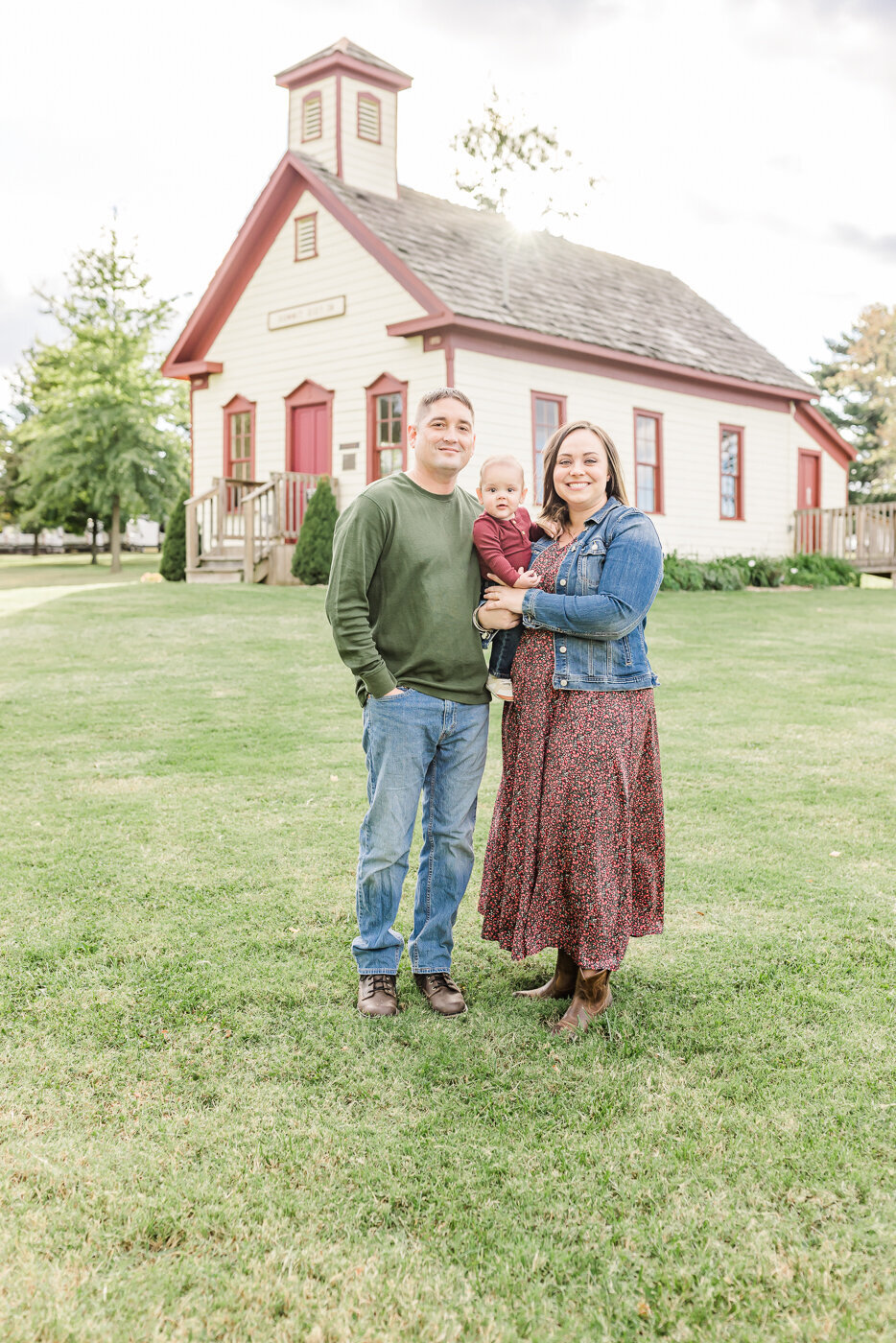 mom and dad pose with their baby boy in front of historical school house at freeman lake
