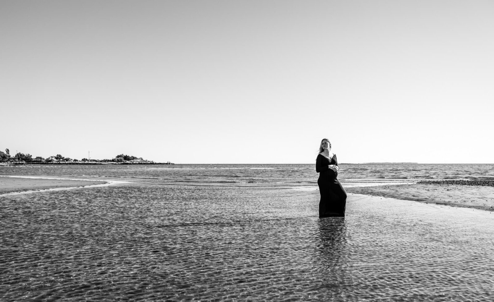 Dramatic black and white photo of pregnant woman in black dress at beach at low tide