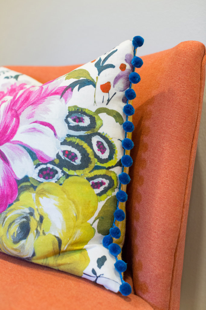 An orange chair with colorful floral throw pillow.