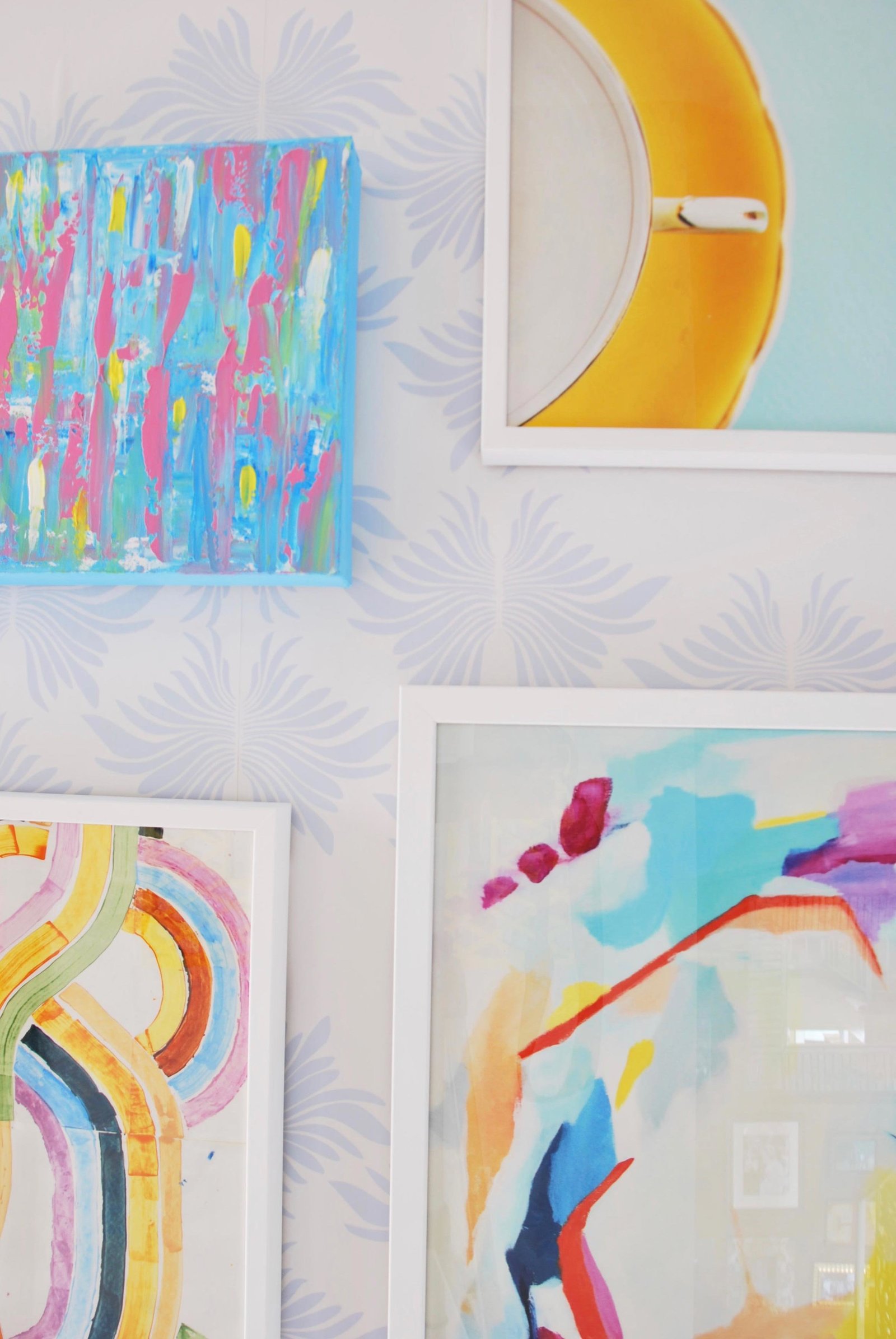 A colorful gallery wall of paintings in white frames.