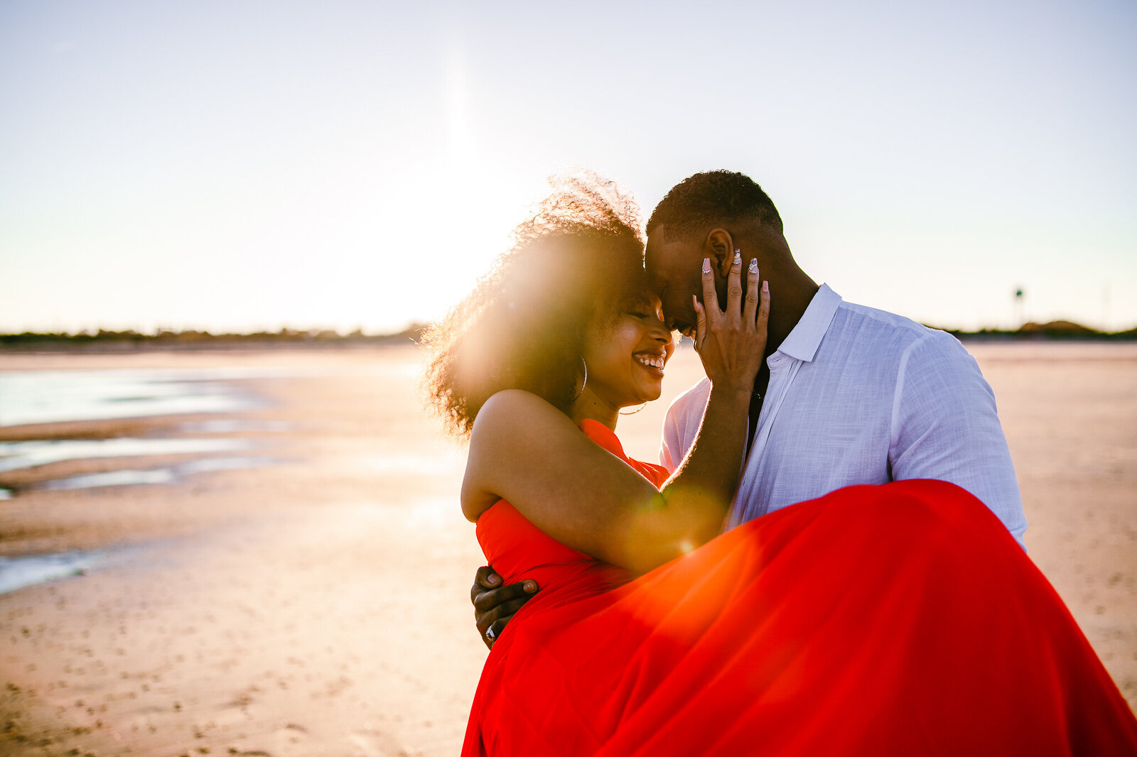 Couples where he is carrying her with sun setting behind them at beach in Tybee Island, GA. Savannah engagements.