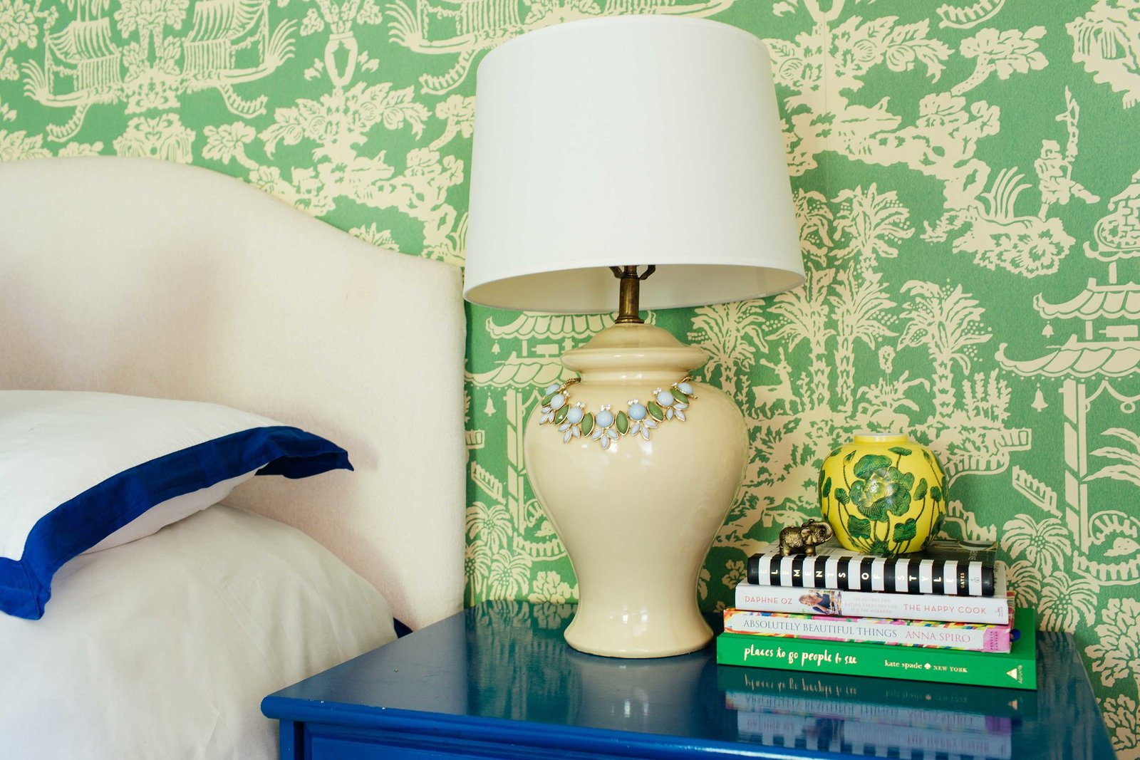 A white bed and blue end table  in front of a green wall papered wall.