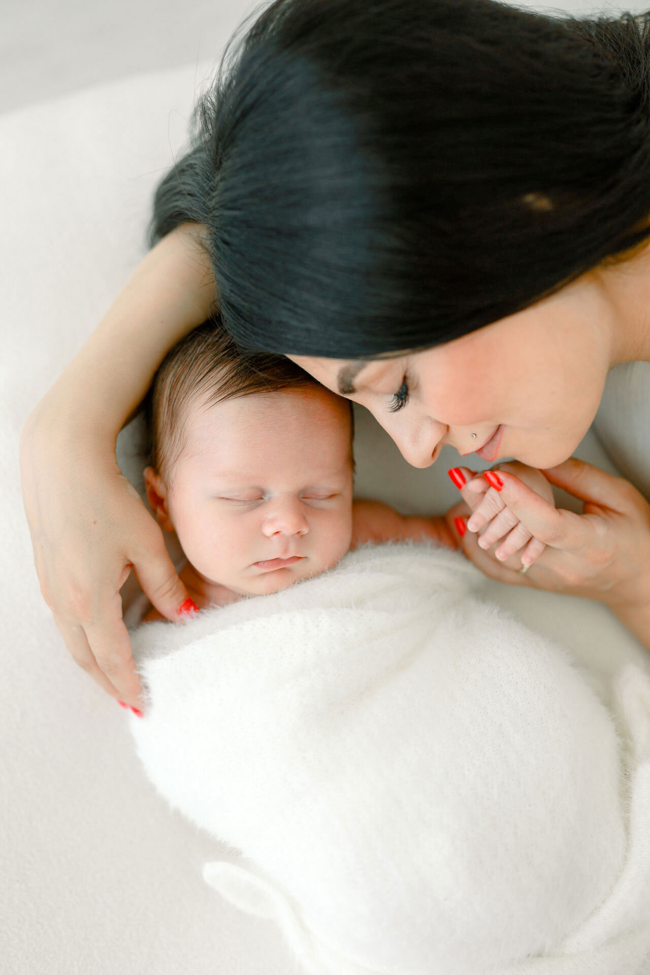 Neugeborenen Fotoshooting bei Verl: Mama hält kleine Hand ihres schlafenden Neugeborenen, das in eine weiße Kuscheldecke eingeschmiegt liegt.