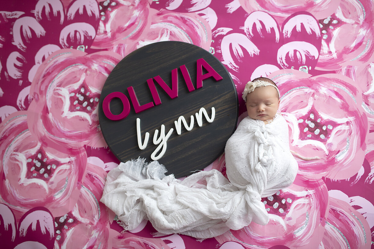 Newborn girl with wooden sign spelling her name, Olivia.