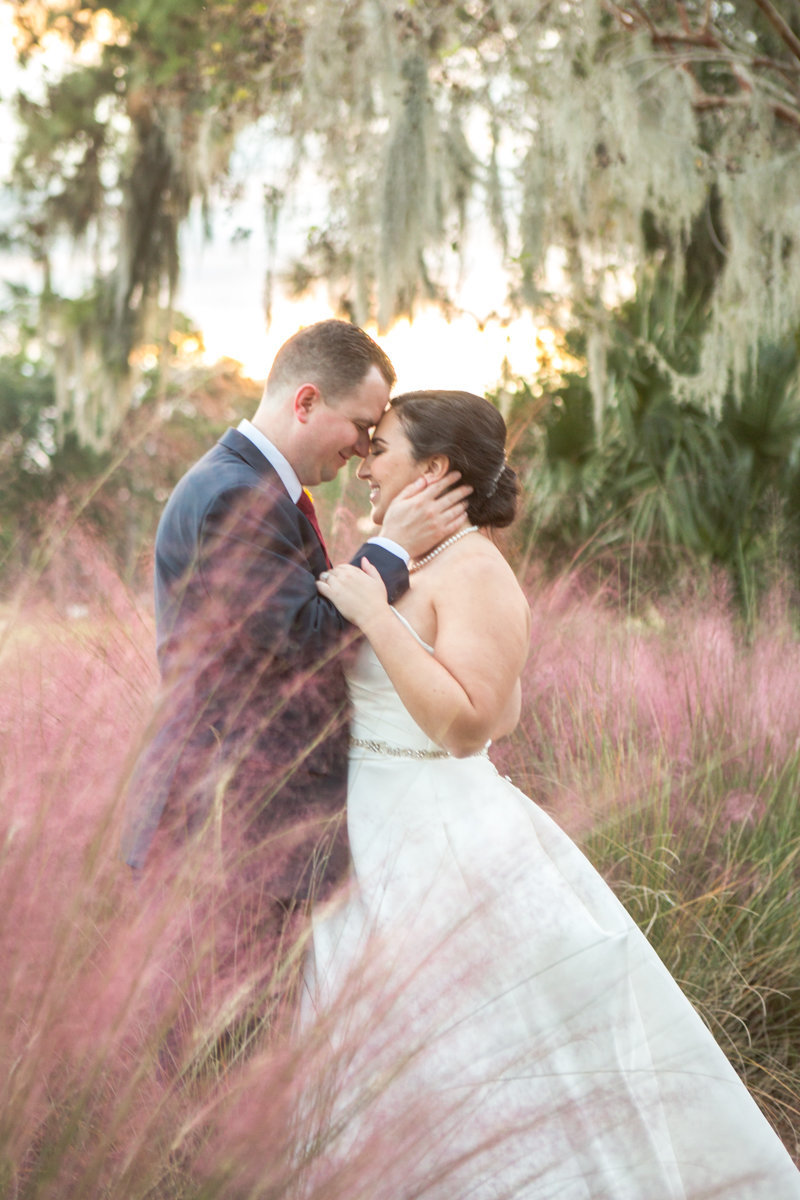 bride and groom touching foreheads in pink fluffy muhly grass