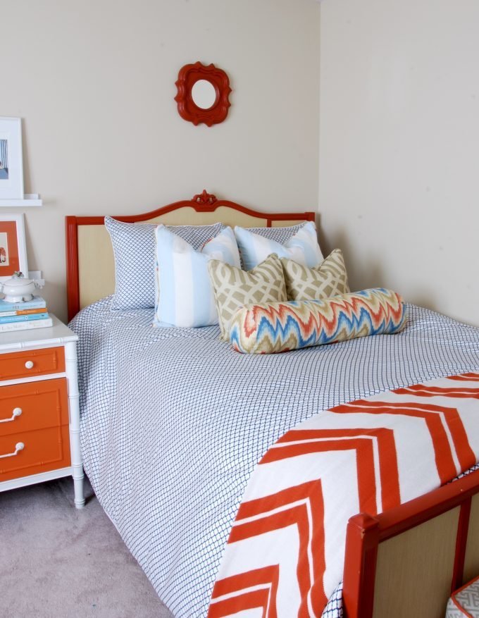 A dark orange and beige bed with a mirror above.