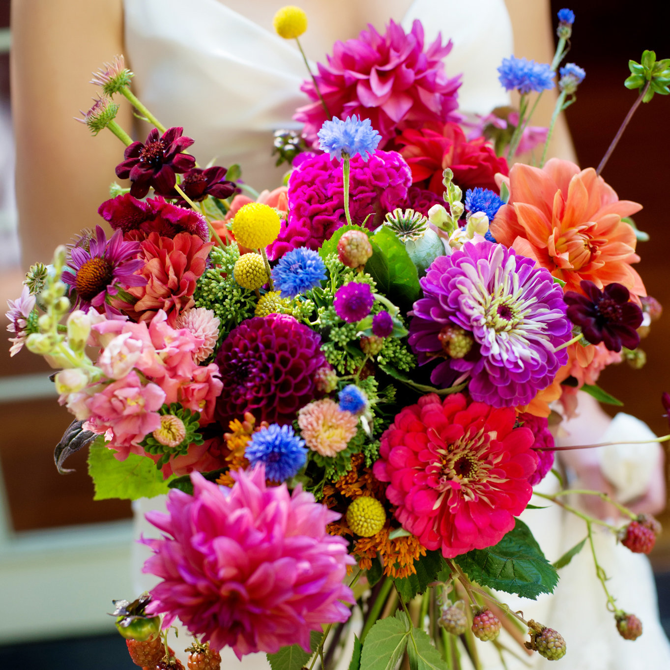 a close up of a bride holding a very colorful and bright wildflower bouquet