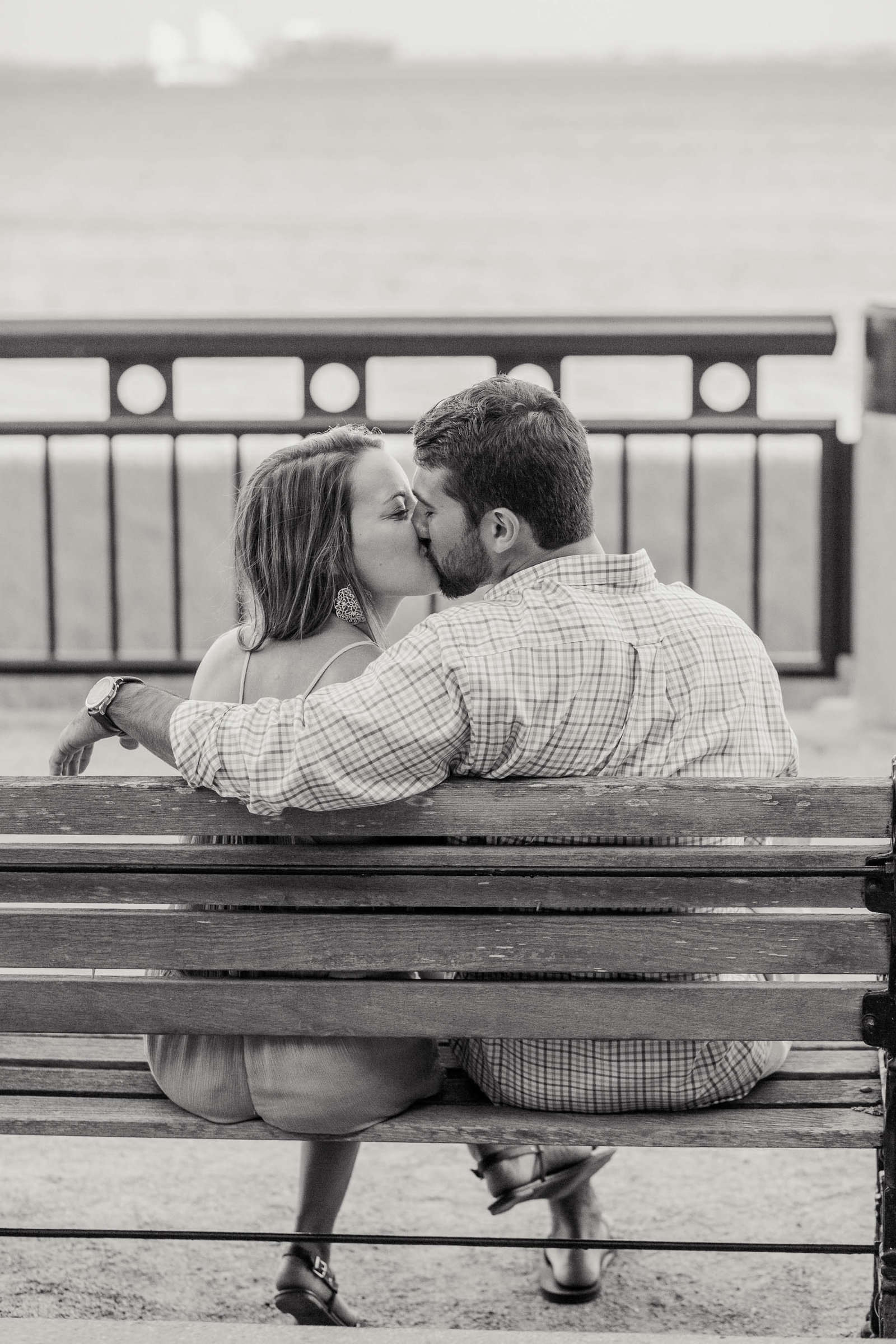 Engaged couple sits on a bench, watching the ocean, Waterfront Park, Charleston, South Carolina