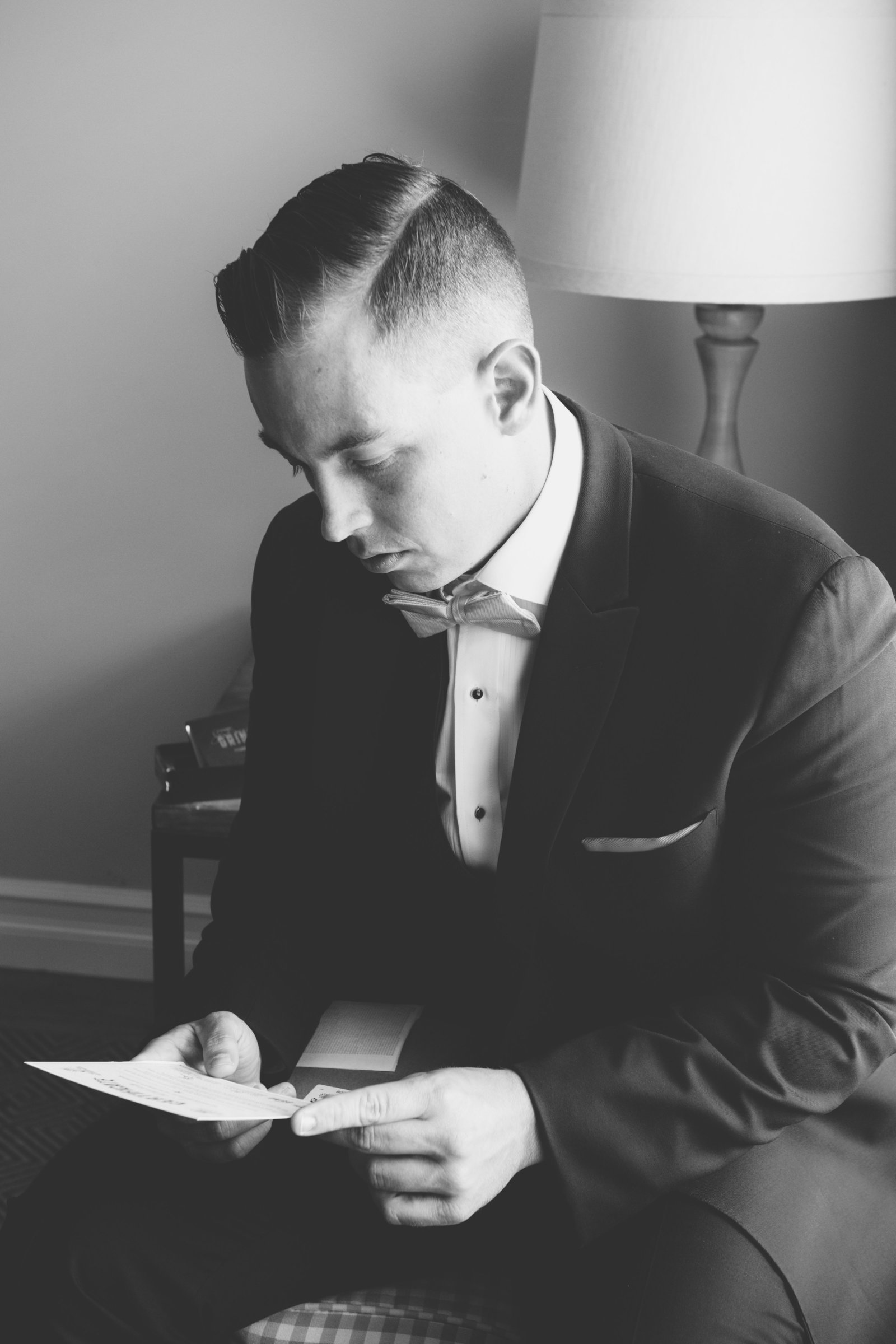 black and white photo of groom reading a note from wedding at Three Village Inn