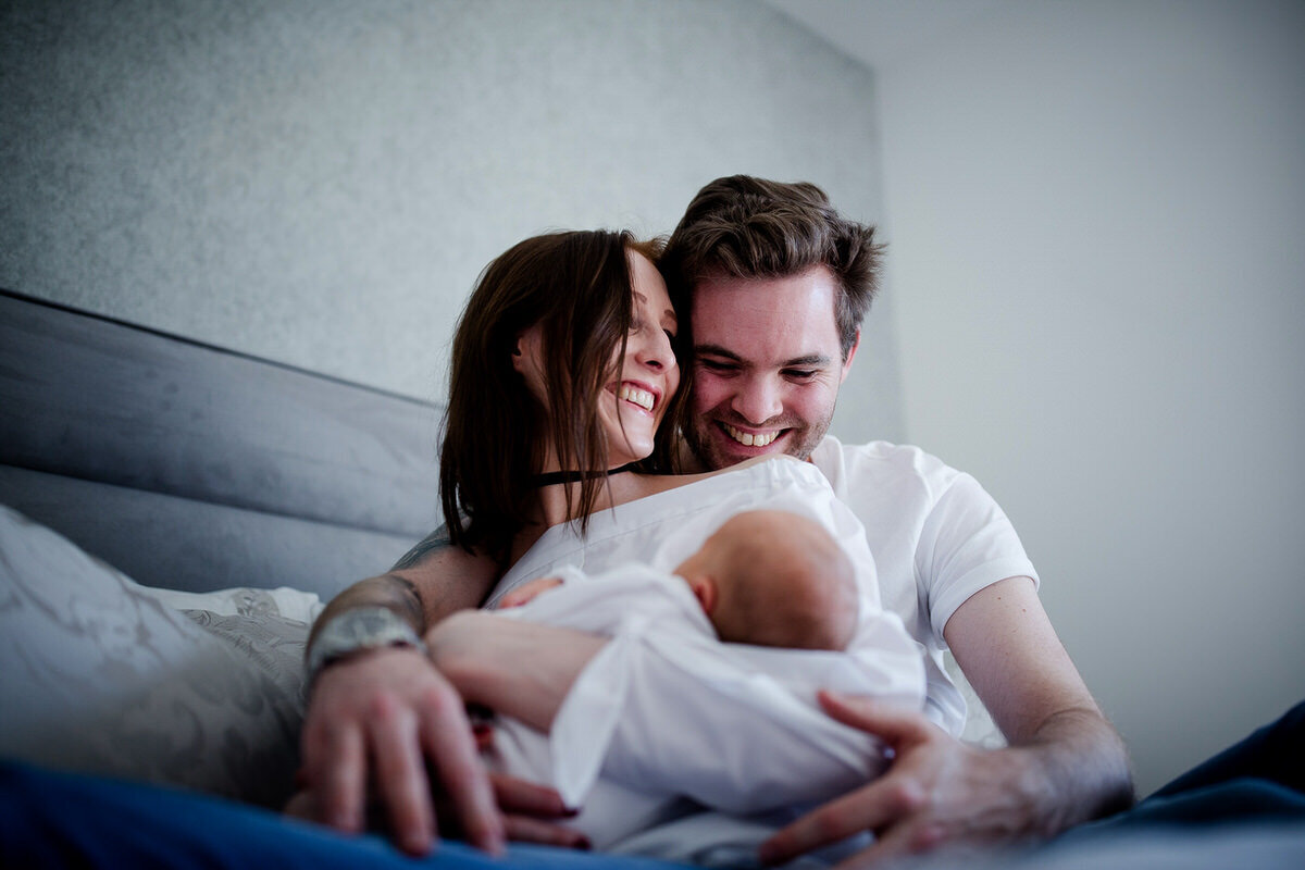Mother and father on a bed smiling whilst holding their newborn child