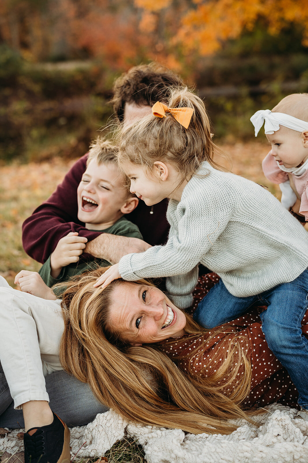 mom laughs while kids jump on top of her during family photos