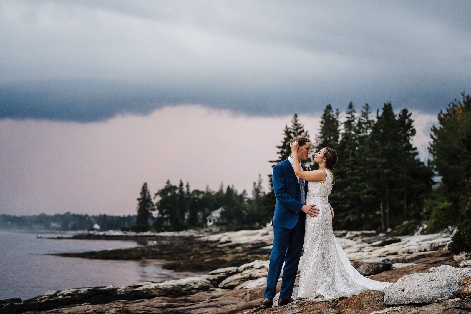 couple stands on ocean rocks under stormy skies