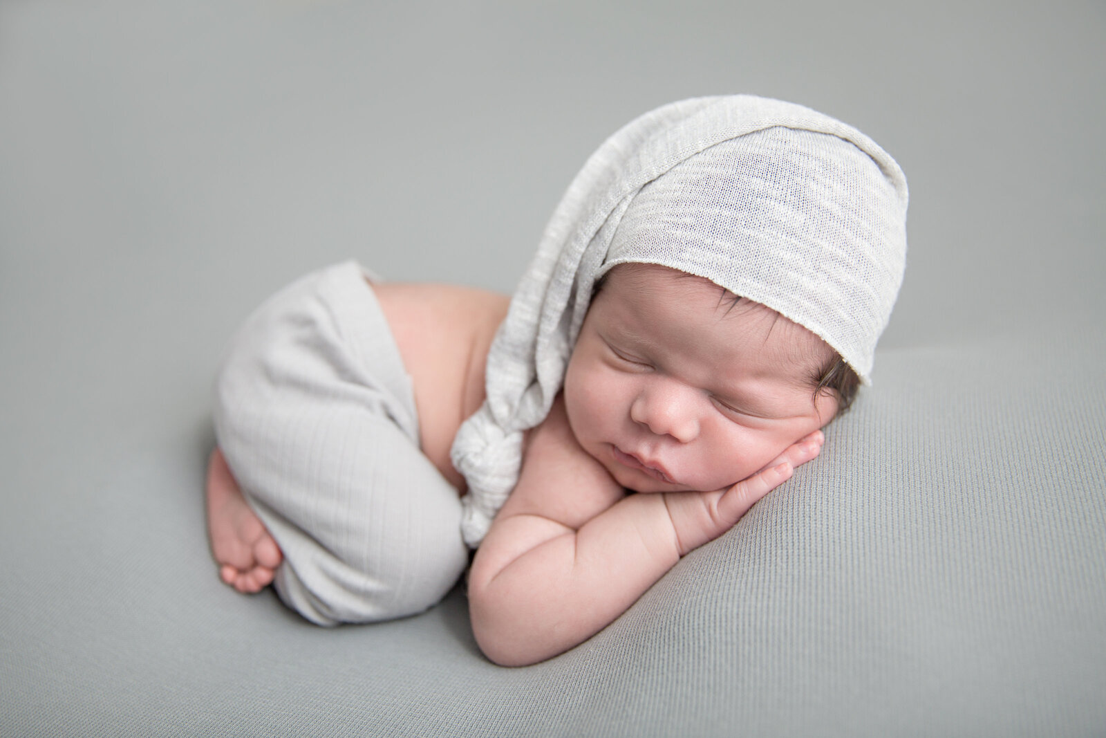sleeping newborn baby in light grey sleepy cap and newborn pants