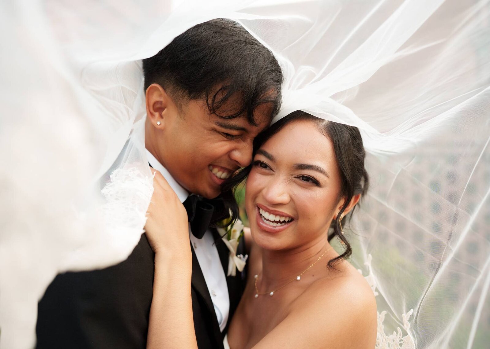 Couple laughs under a veil before their wedding reception
