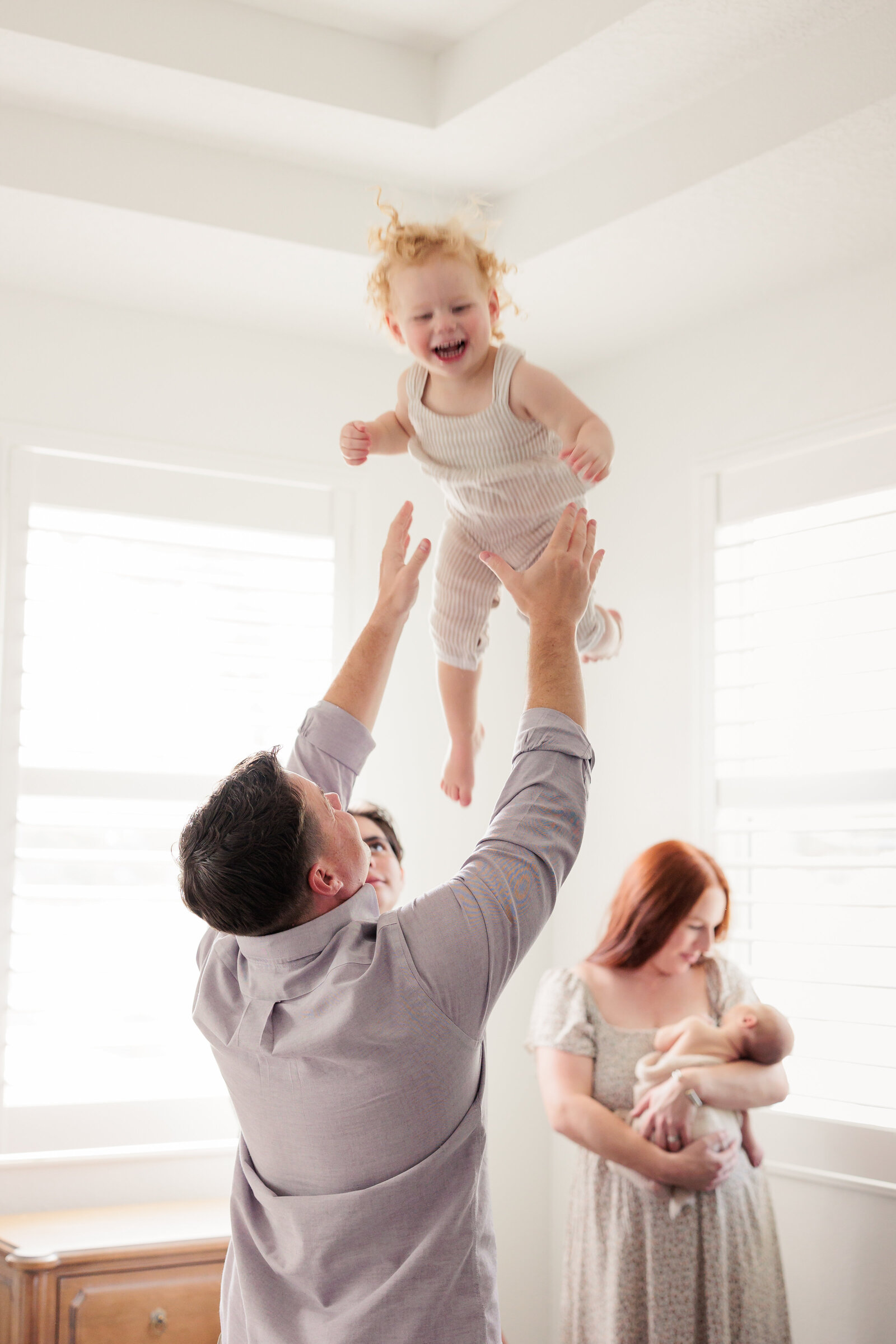 Dad tosses his little girl in the air while mom snuggles her new little brother in the background