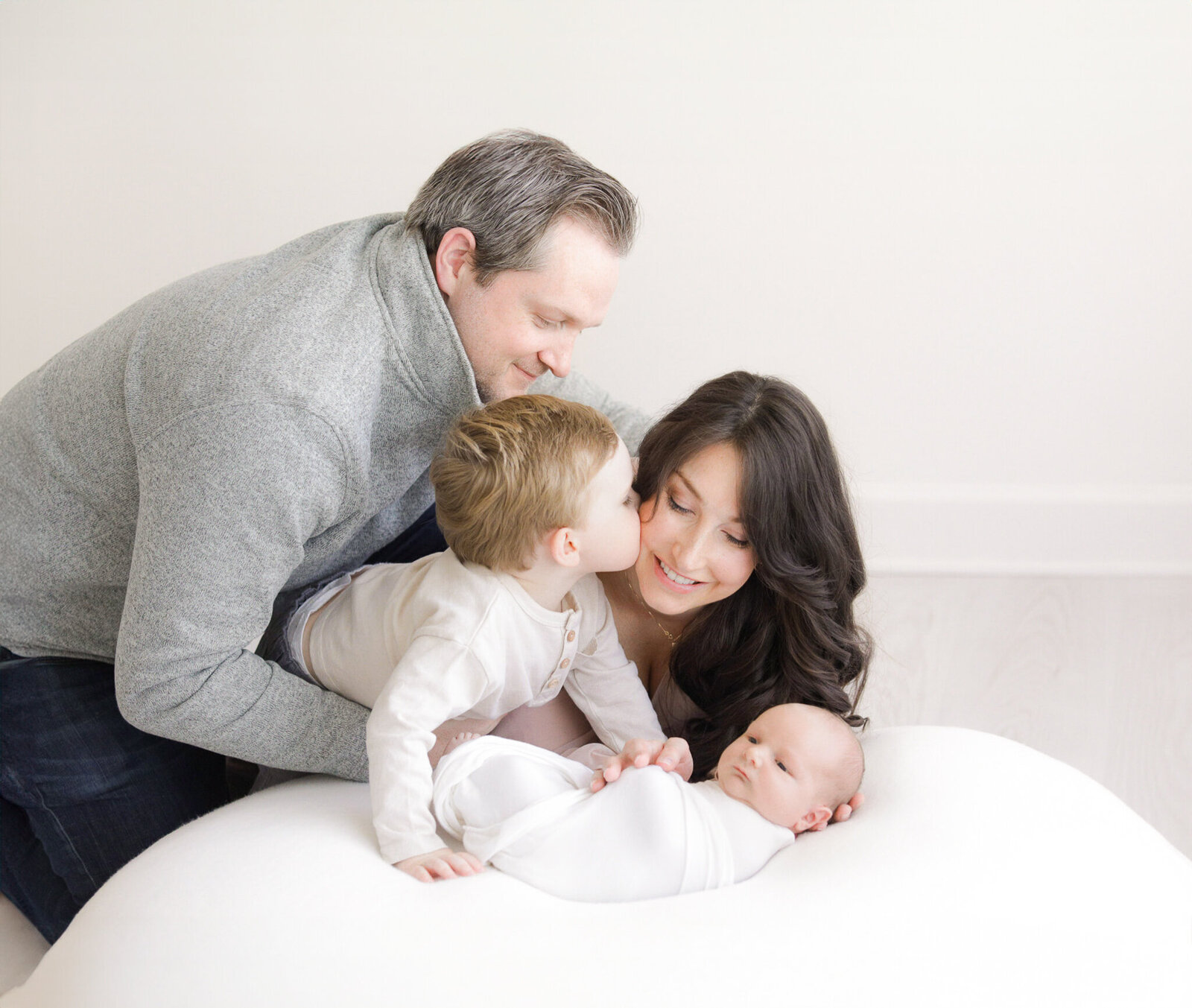 toddler kisses mom on the cheek while dad looks on and newborn baby lays on beanbag during connecticut newborn sessions