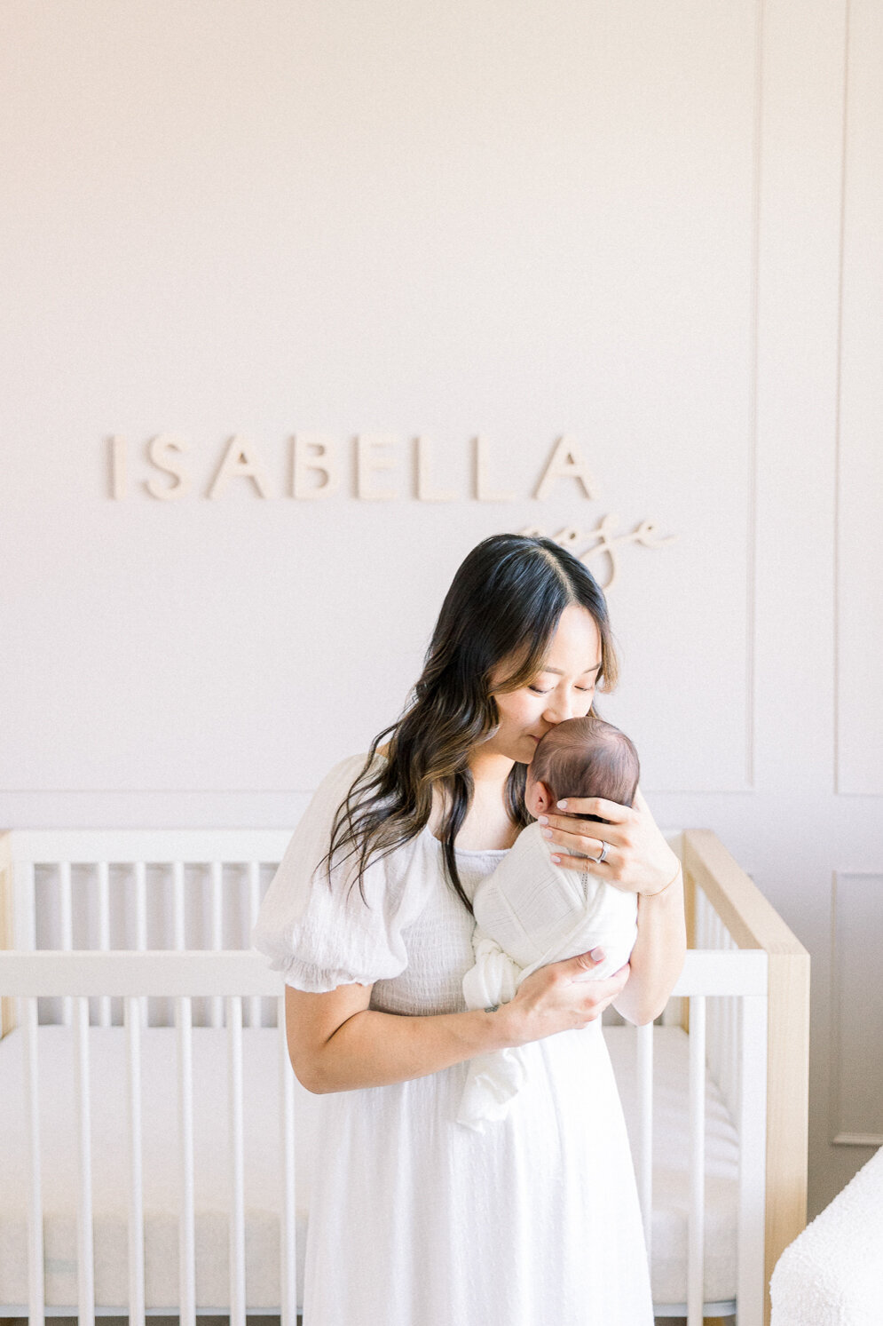 Image of mother kissing baby standing in nursery taken by Sacramento Newborn Photographer Kelsey Krall