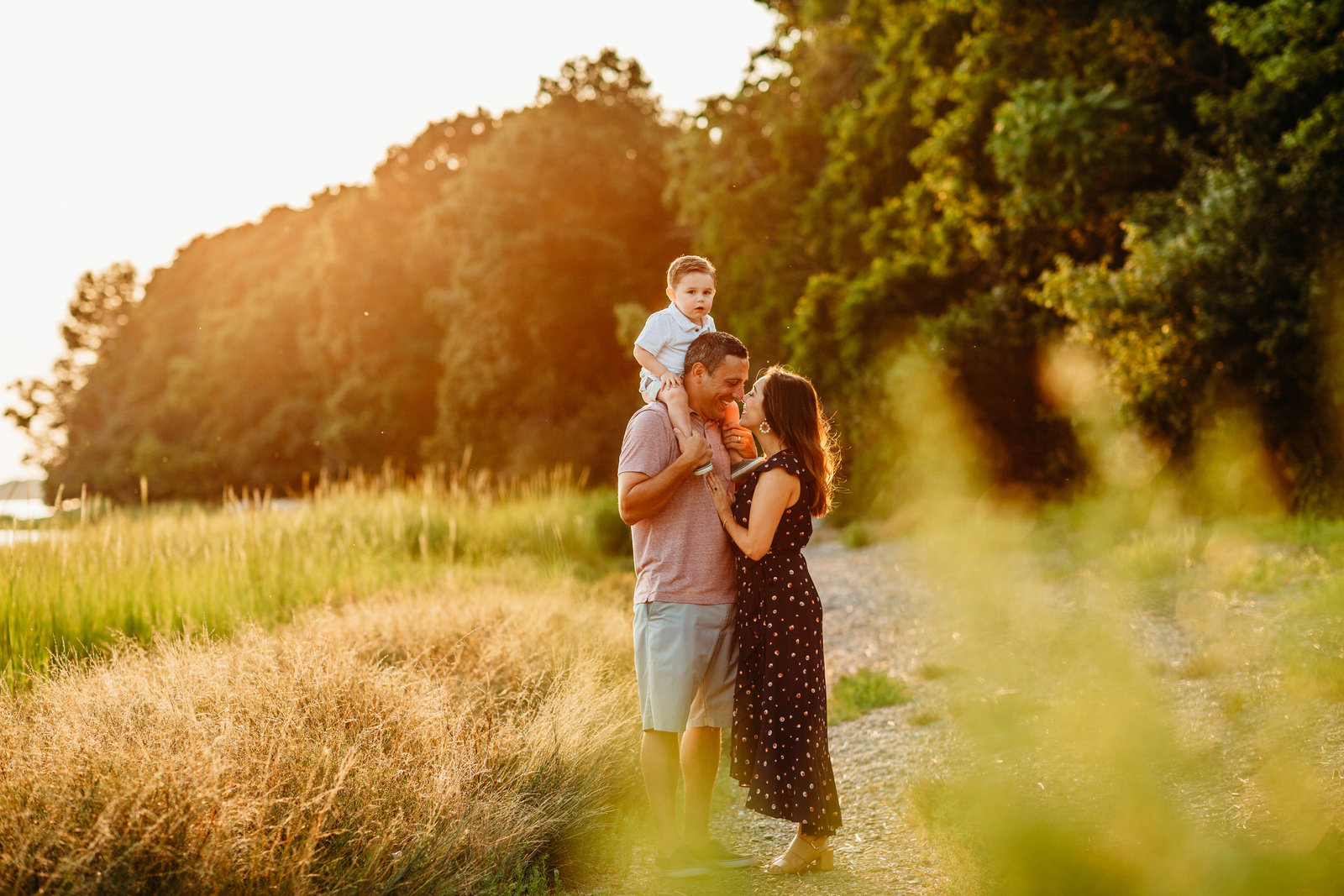 family stands in sunset field with boy on shoulders during family photo session in weymouth ma