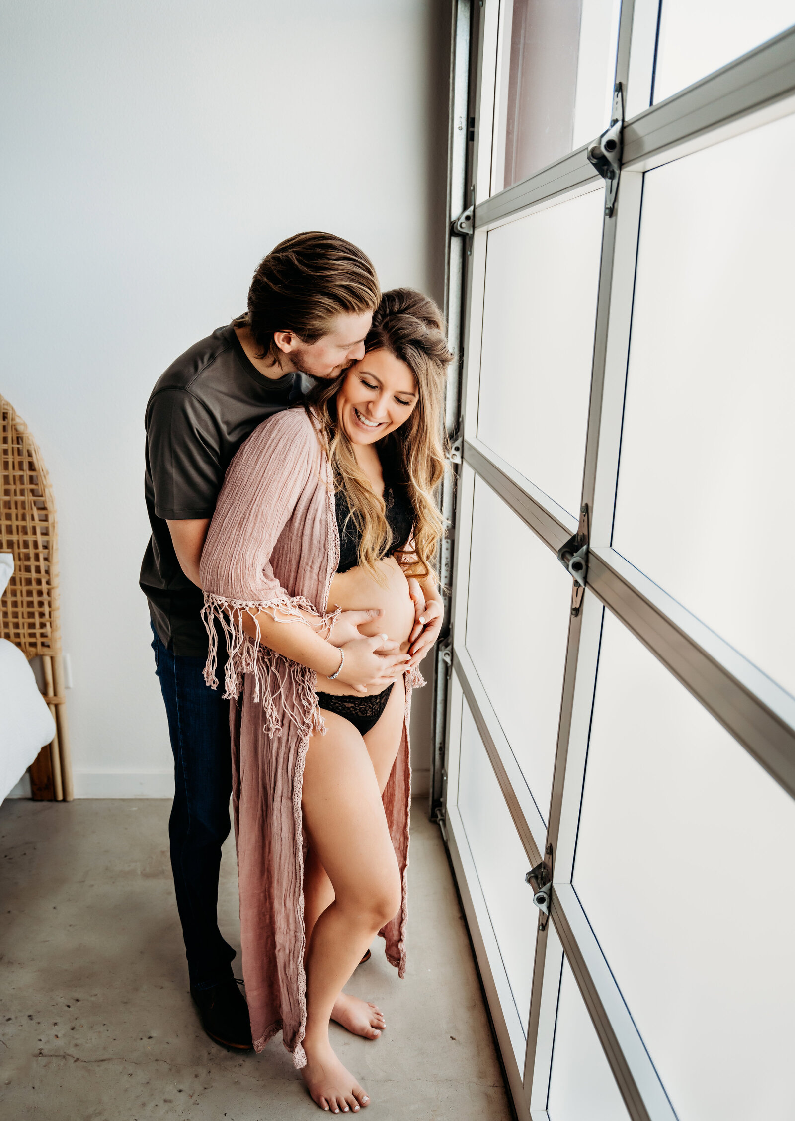 Maternity Photographer, a man hugs his wife from behind, she is pregnant baby, they stand in their loft