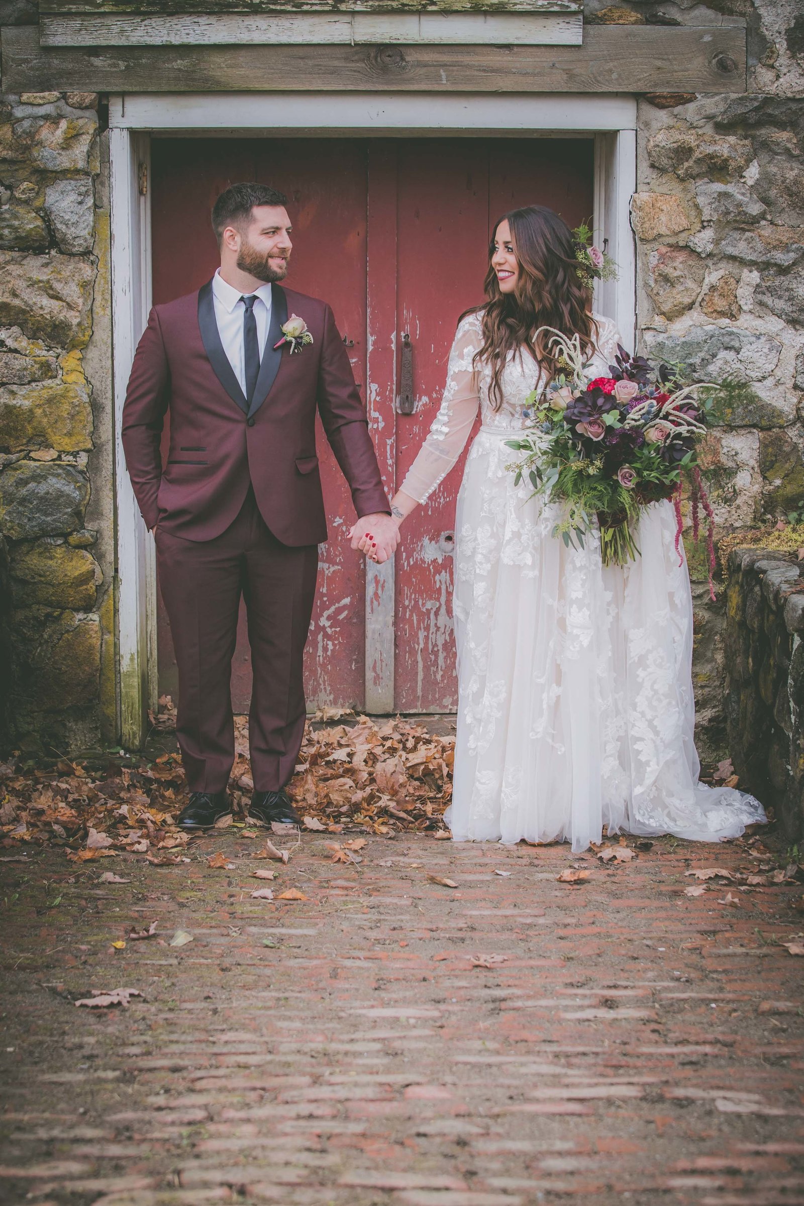 Groom and bride hold hands against a red door.