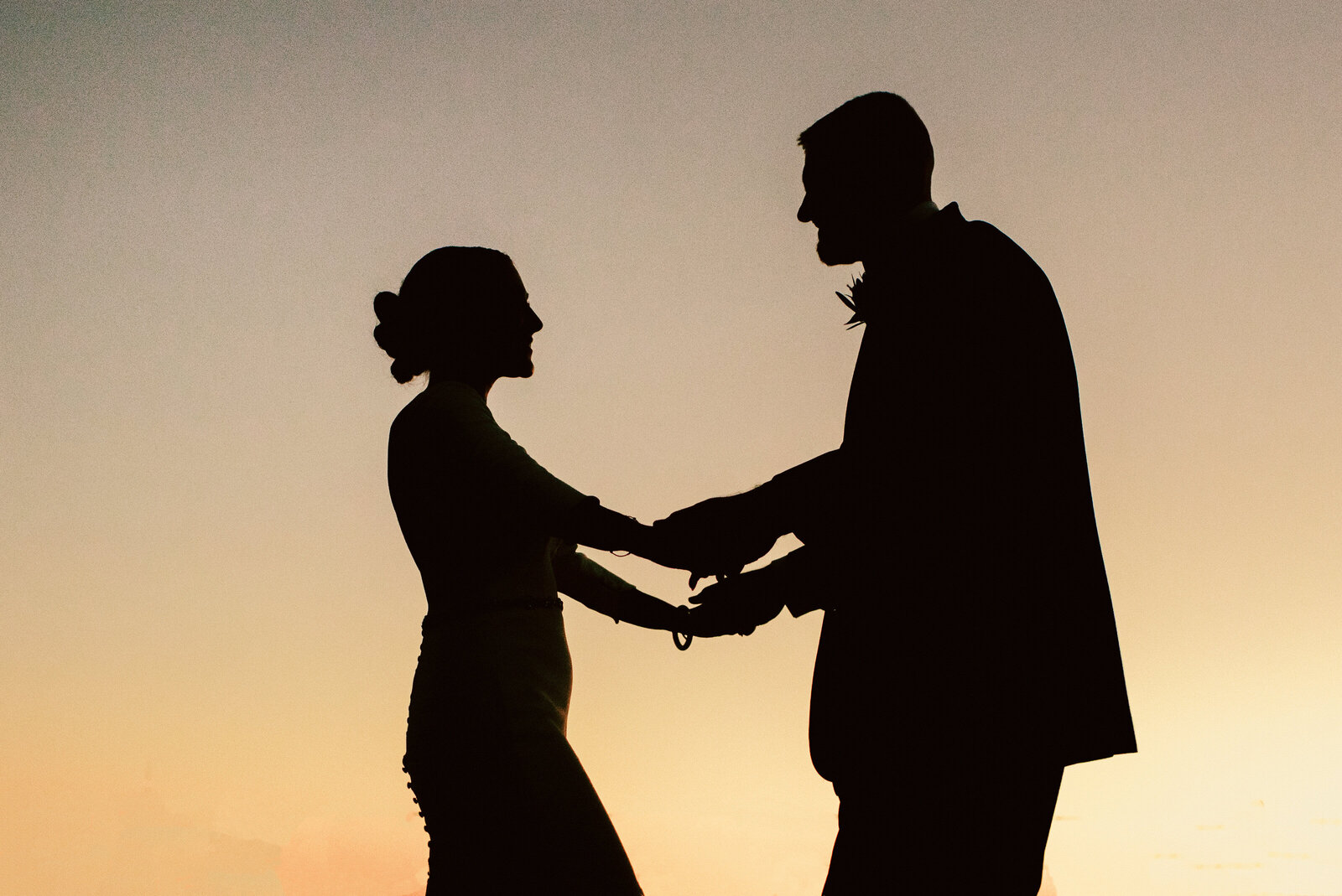 silhouette of man and woman holding hands and dancing at sunset on their wedding day