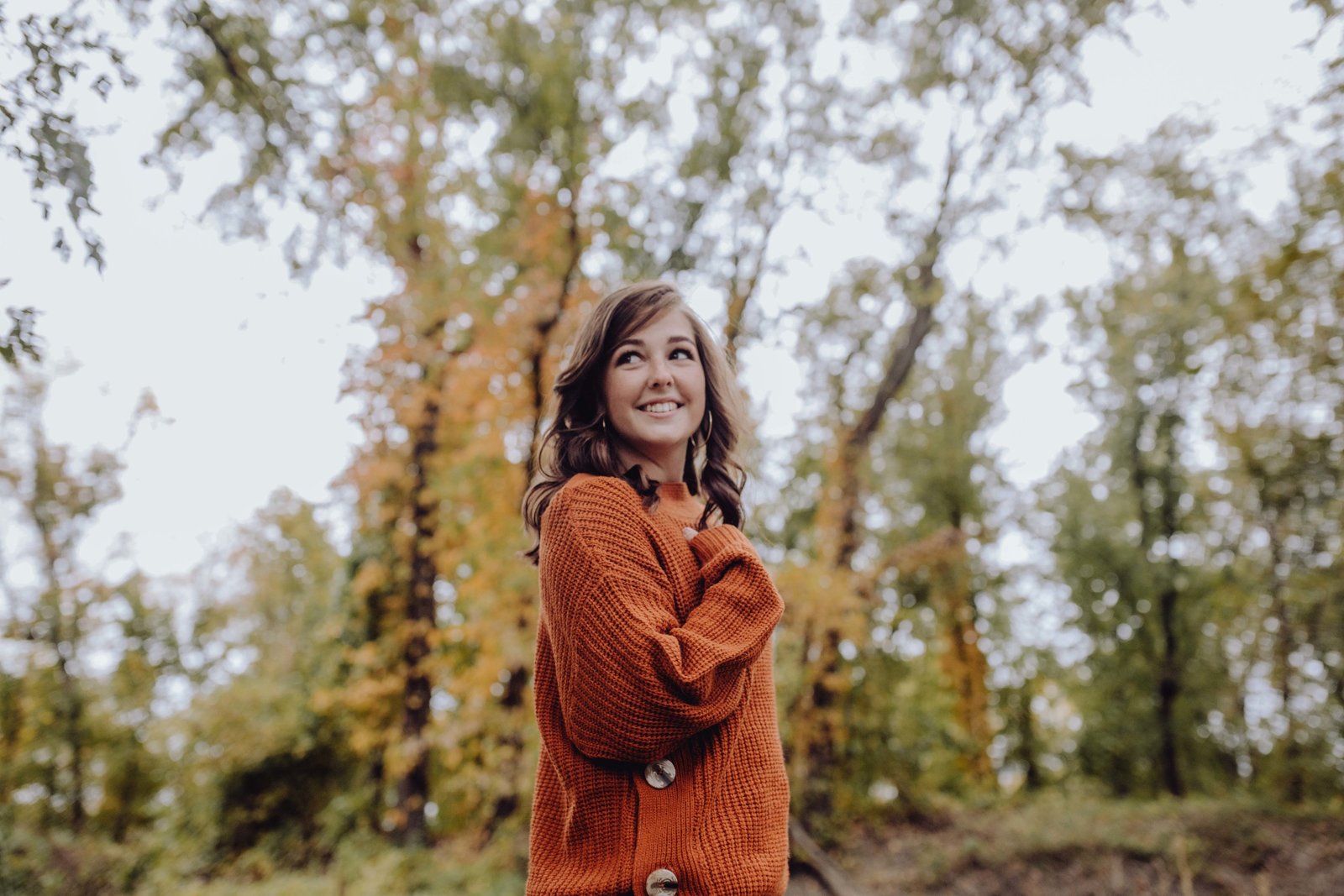 Girl wearing orange sweater, holding hand to chest and looking up with a smile on her face.