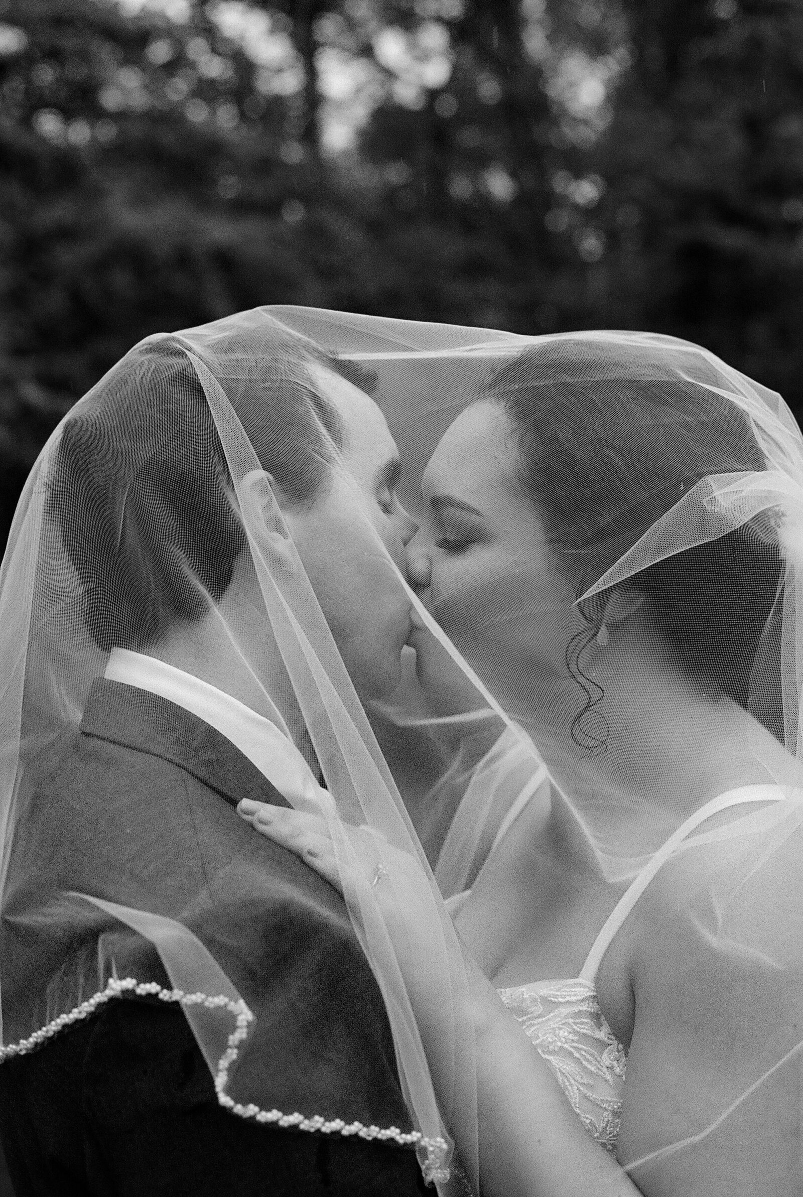Black and white film image of a bride and groom kissing under their veil in Maryland