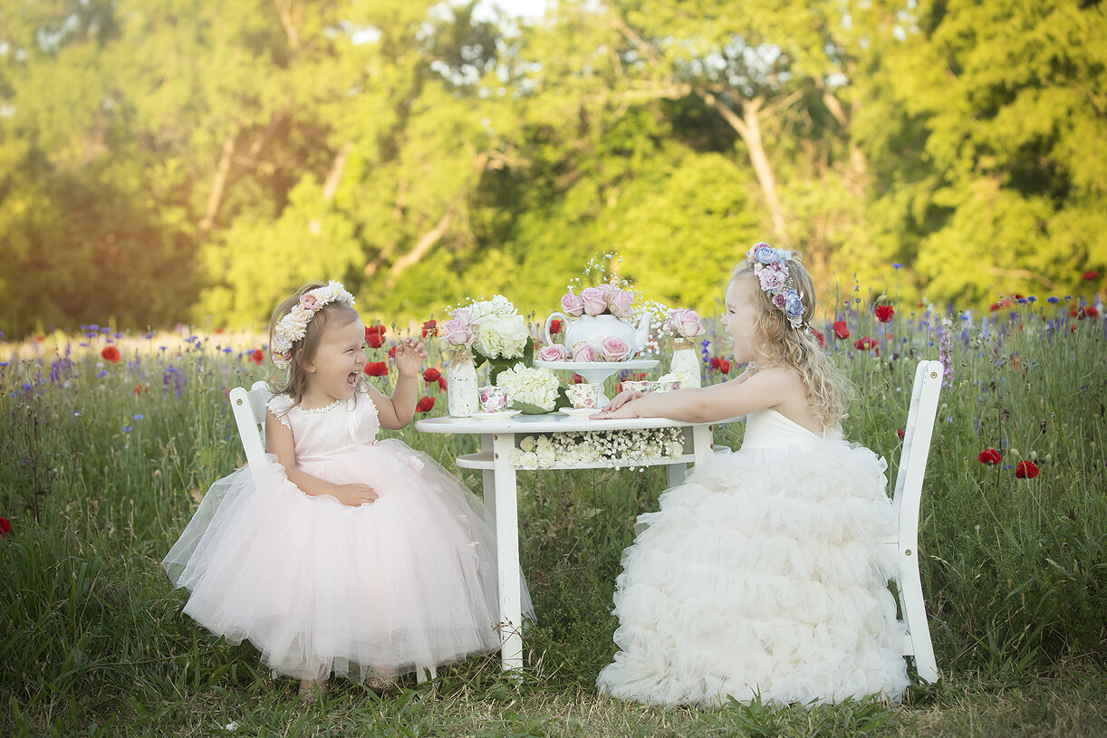 Two girls at tea party in wildflower field.