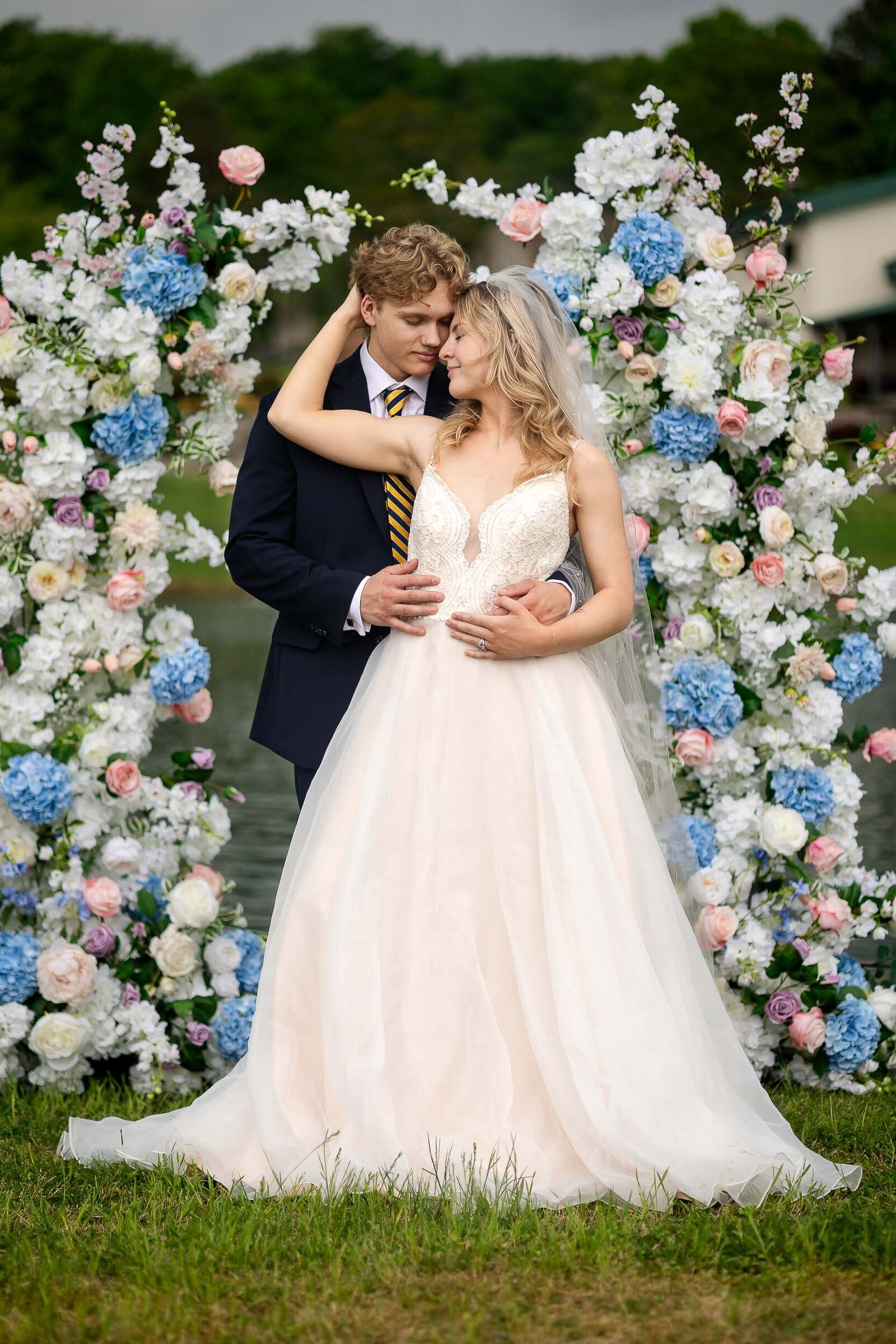 Couple embraces under a stunning floral arch at Willow Tree Farms