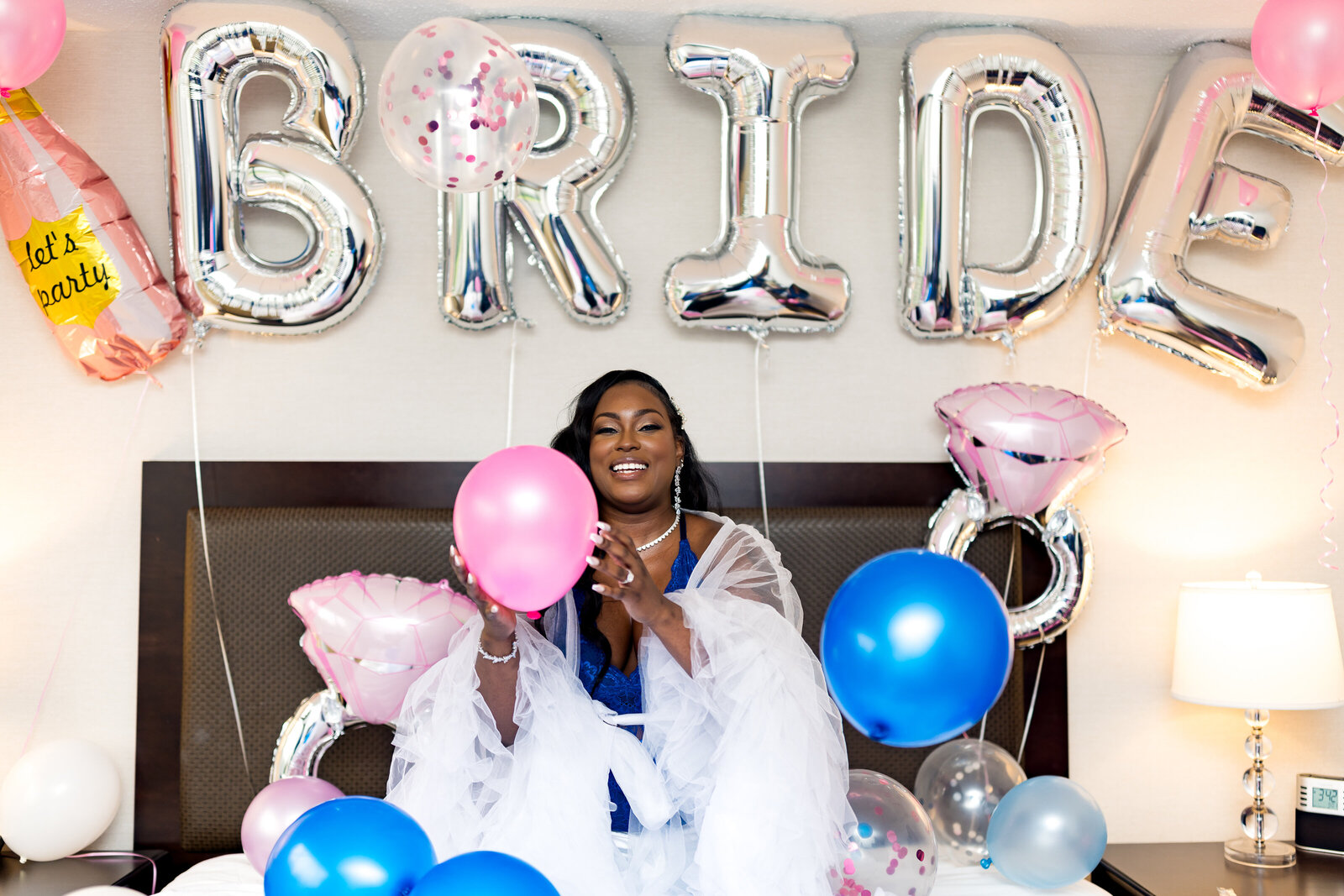 The black bride is posing with balloons on the bed happy.