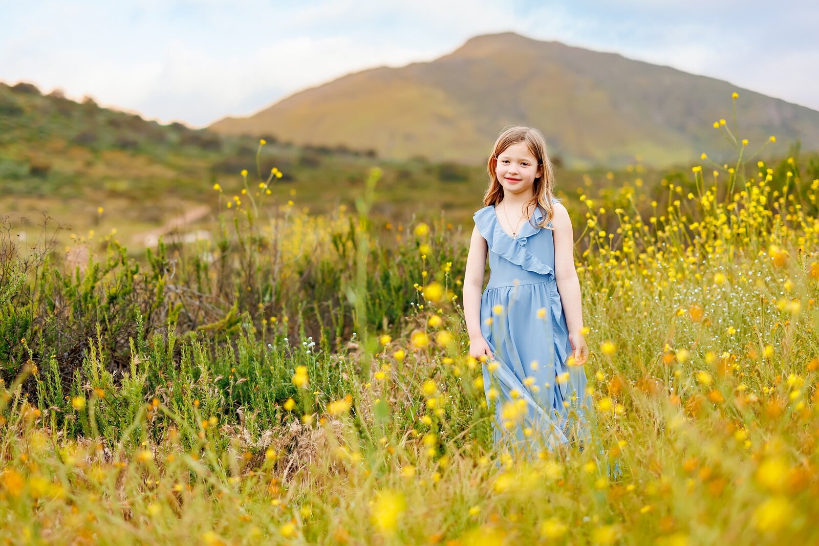 Portrait of girl wearing a blue dress among wildflowers and a mountain in the background in north county San Diego