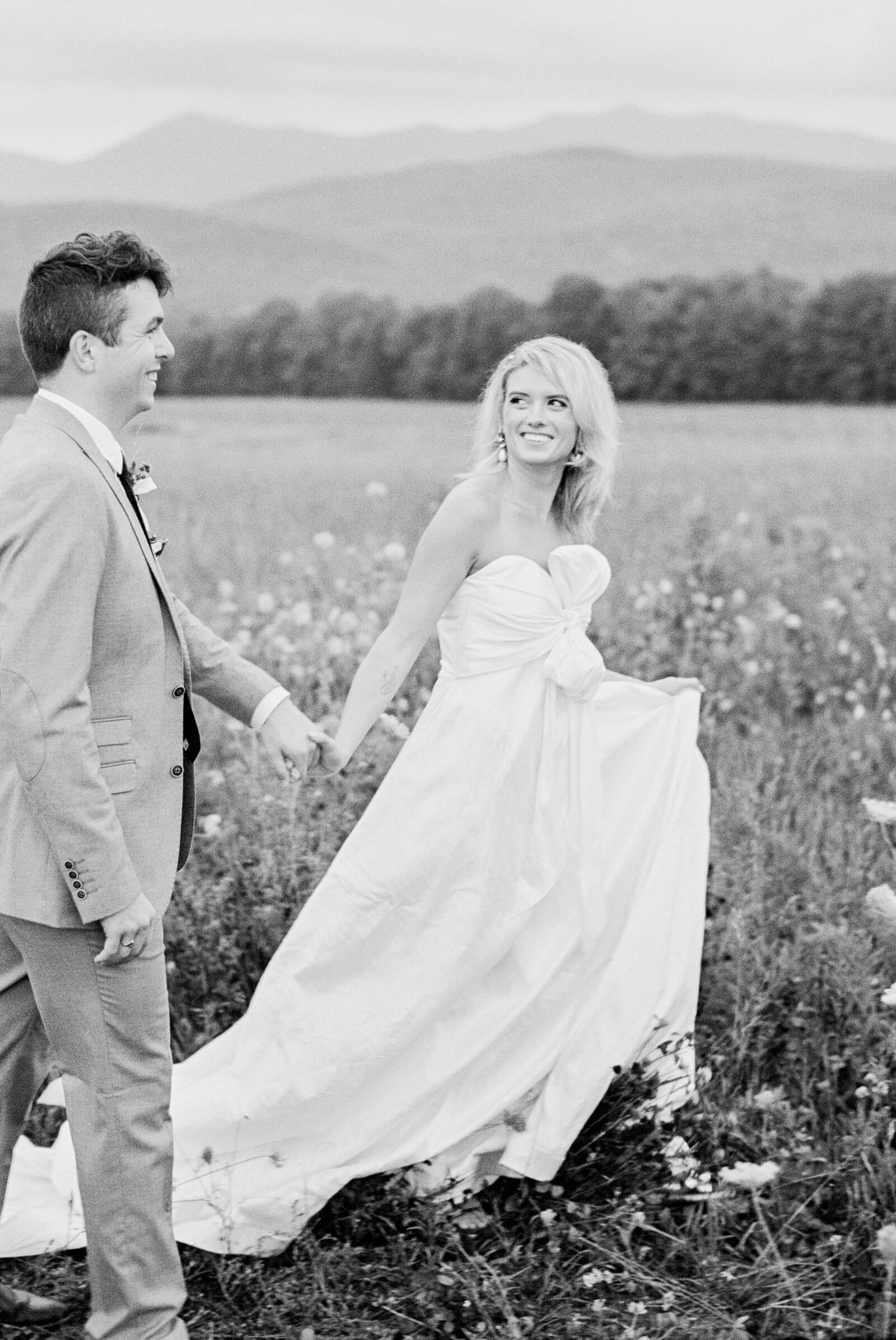 Black and white photo of a wedding couple walking through a field.