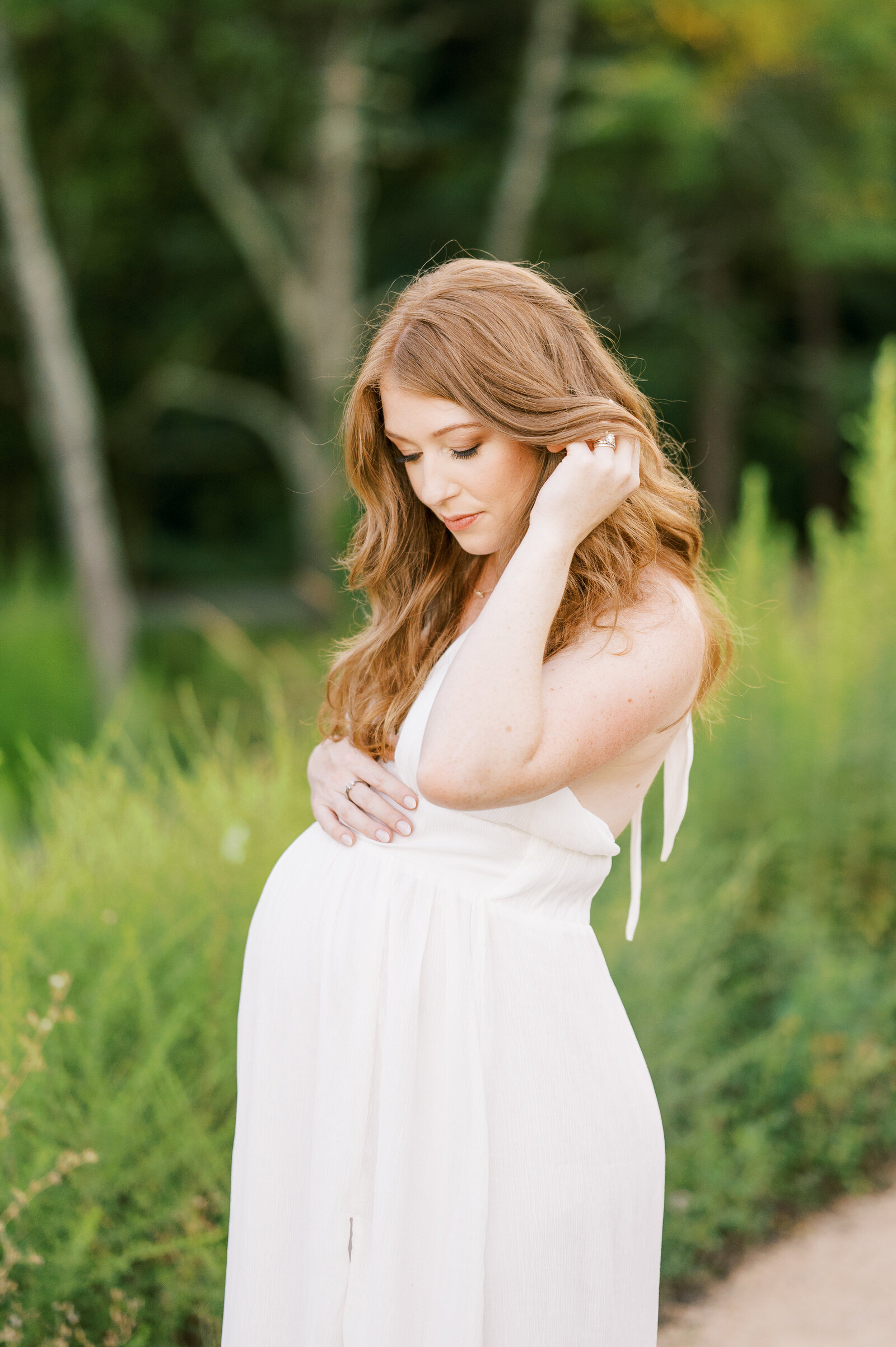 Expecting mom in white dress pulls hair back during maternity photoshoot