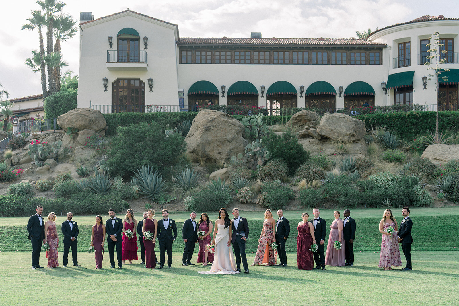 Full wedding party stands in front of terracotta archways and hills of Simi Valley, captured in editorial film style.