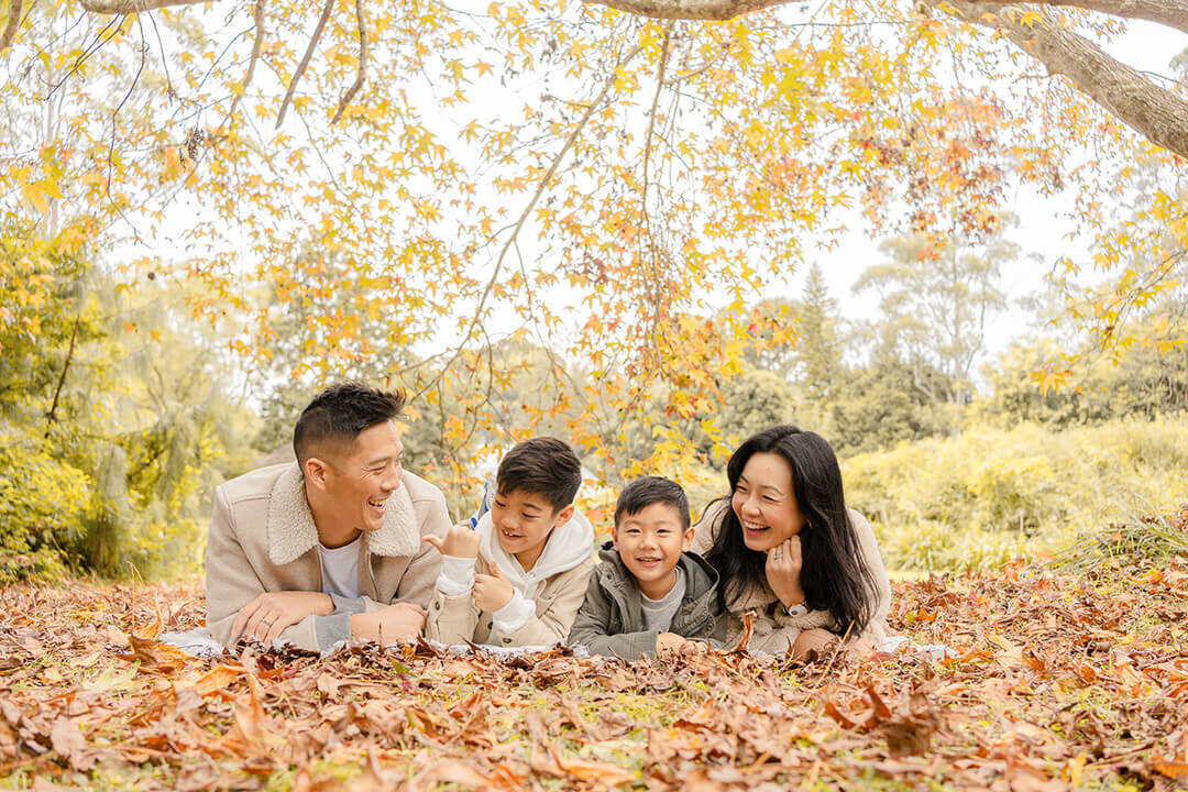 candid family photography of 4 lying on carpet of autumn leaves laughing, captured by family photographer hikari
