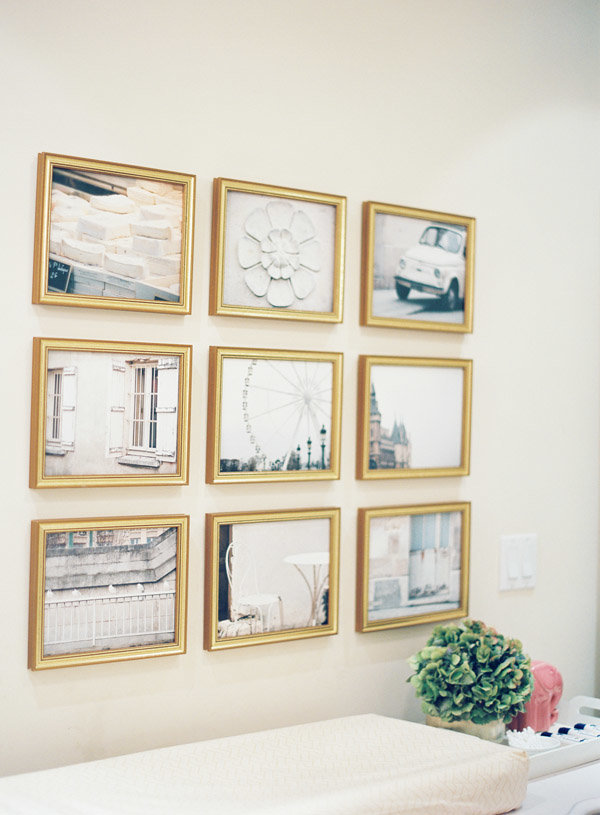 A grid gallery wall of fine art and photos above a changing table.